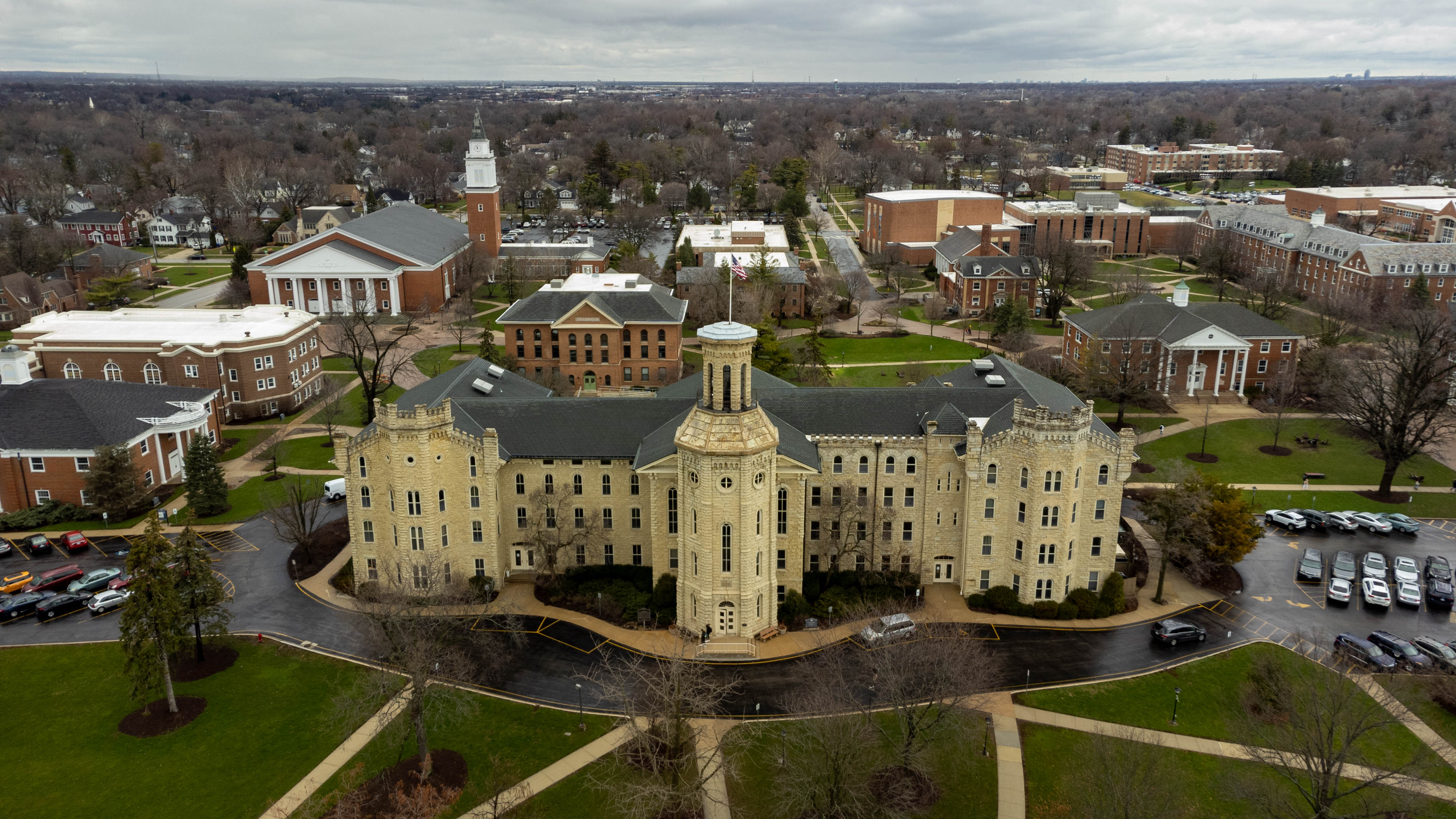Aerial drone view of a historic stone building with a cupola on a college campus.