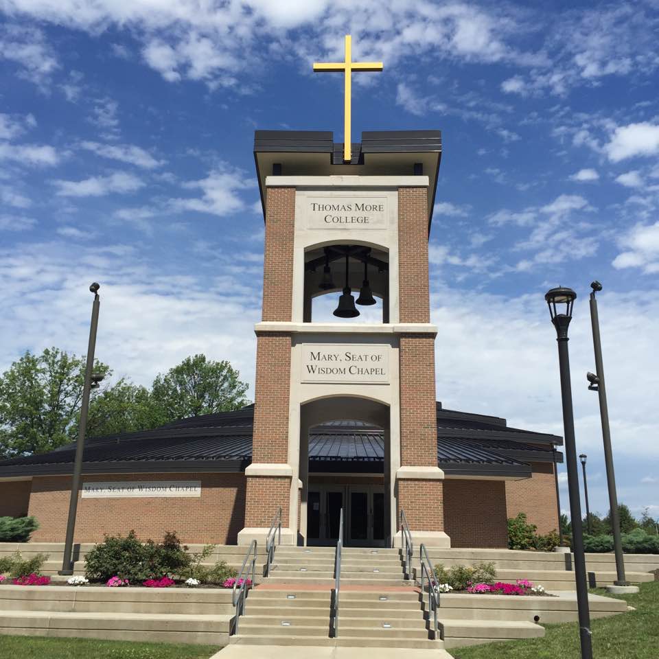 Brick bell tower and chapel entrance at a university campus with a gold cross on top.