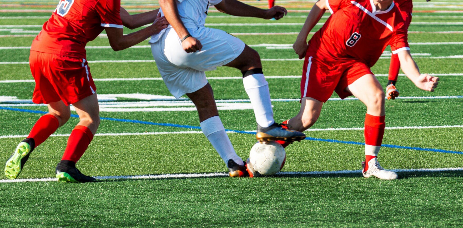Three youth soccer players compete for a ball on an artificial turf field.