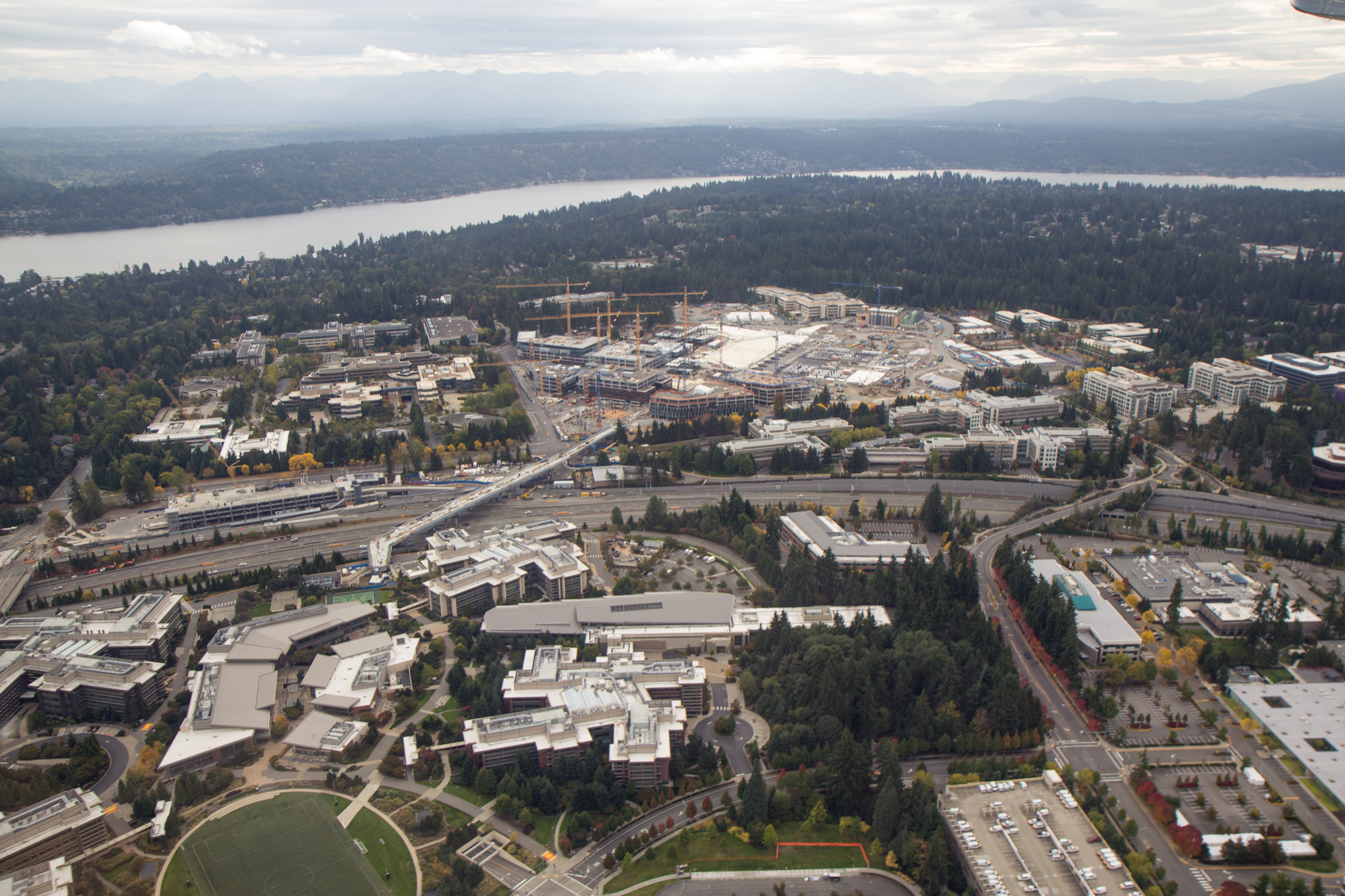Aerial view of a large corporate campus with office buildings, roads, and a lake in the background.