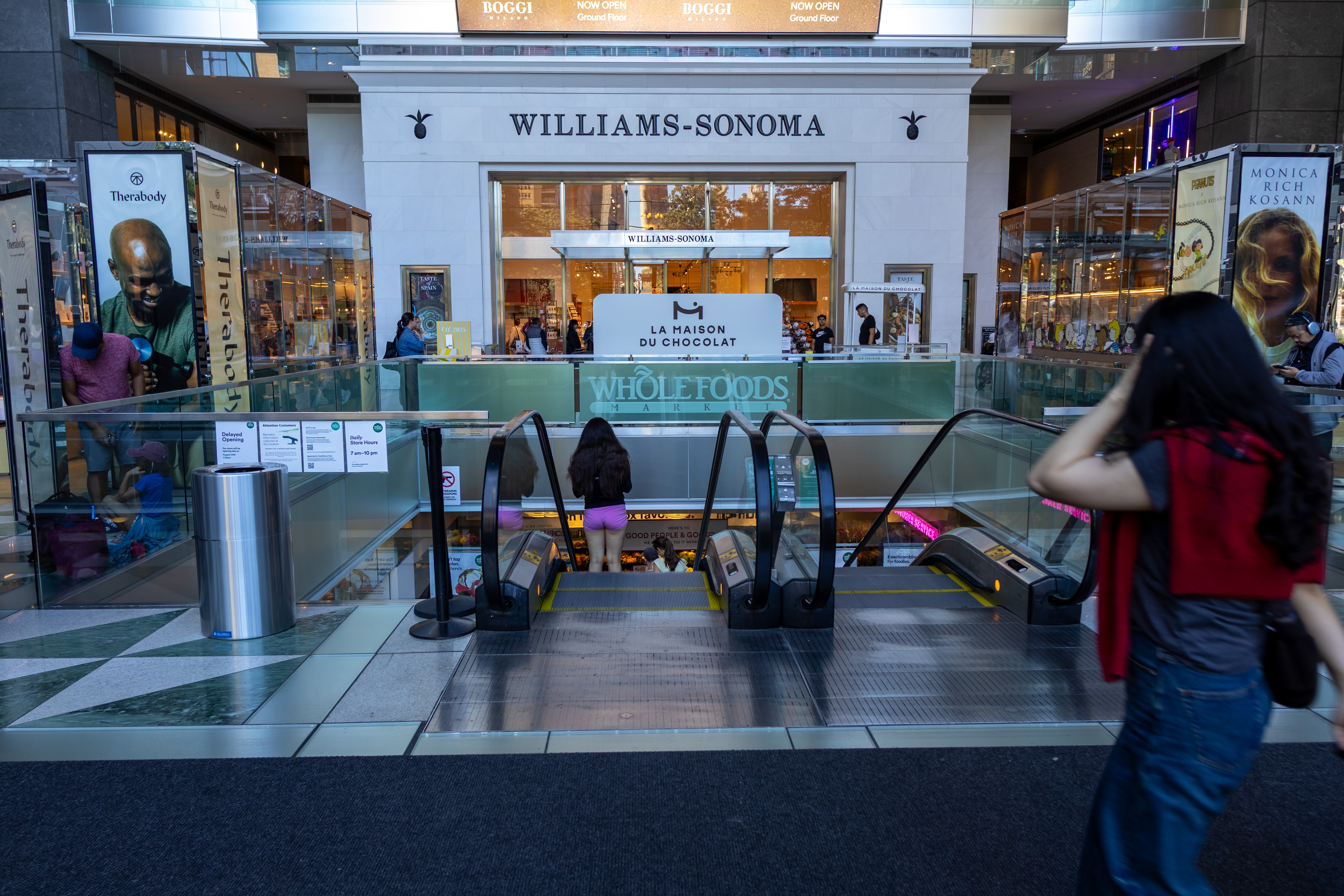 Escalators descend toward a Whole Foods Market store entrance inside a shopping mall.