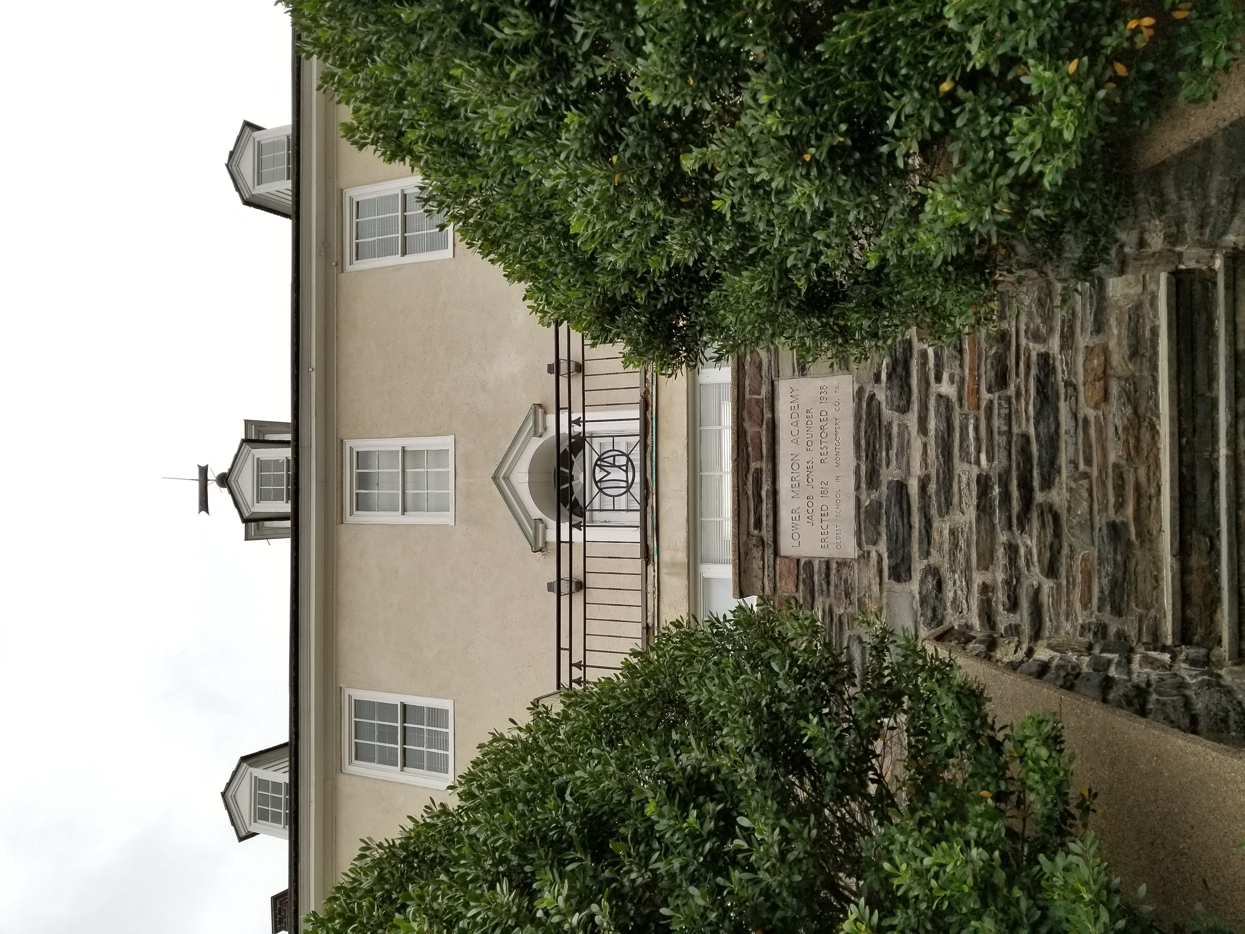 Stone plaque on the wall of a historic Georgian-style school building with stone steps and trimmed hedges.