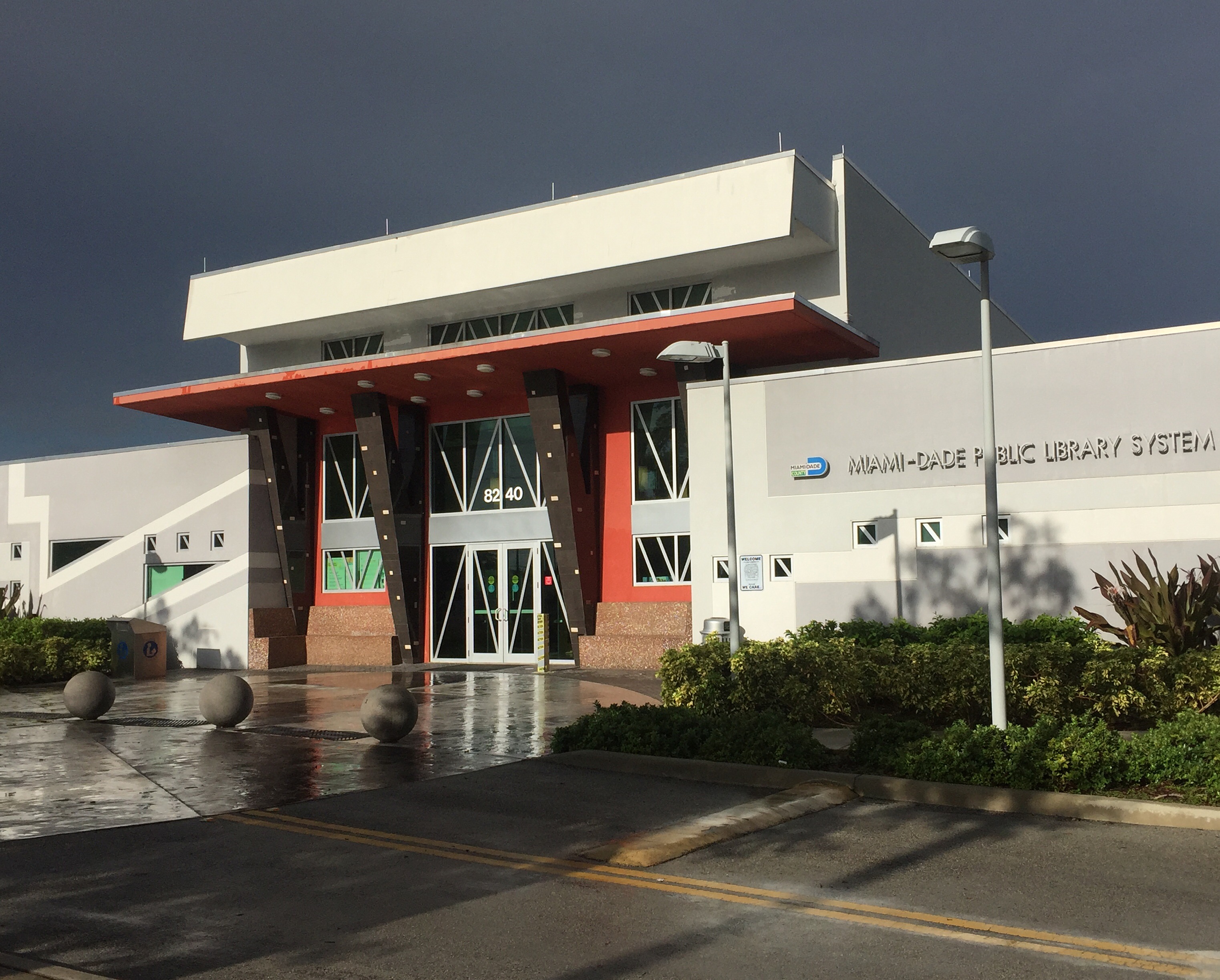 Exterior of a Miami-Dade Public Library System branch with red entrance canopy and signage.