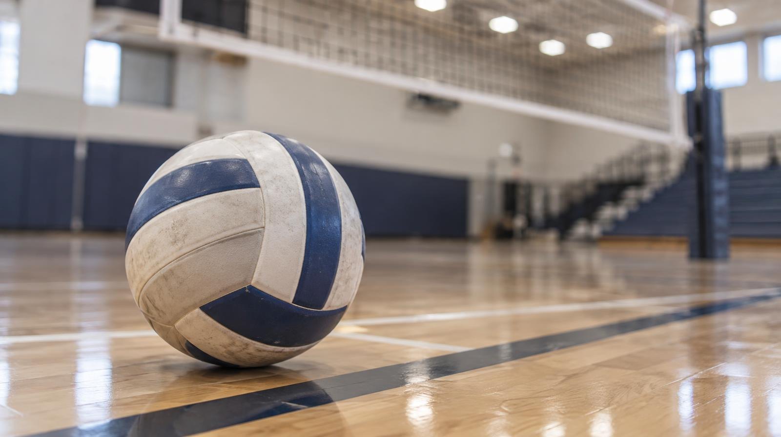A volleyball resting on a hardwood gym floor near the net.