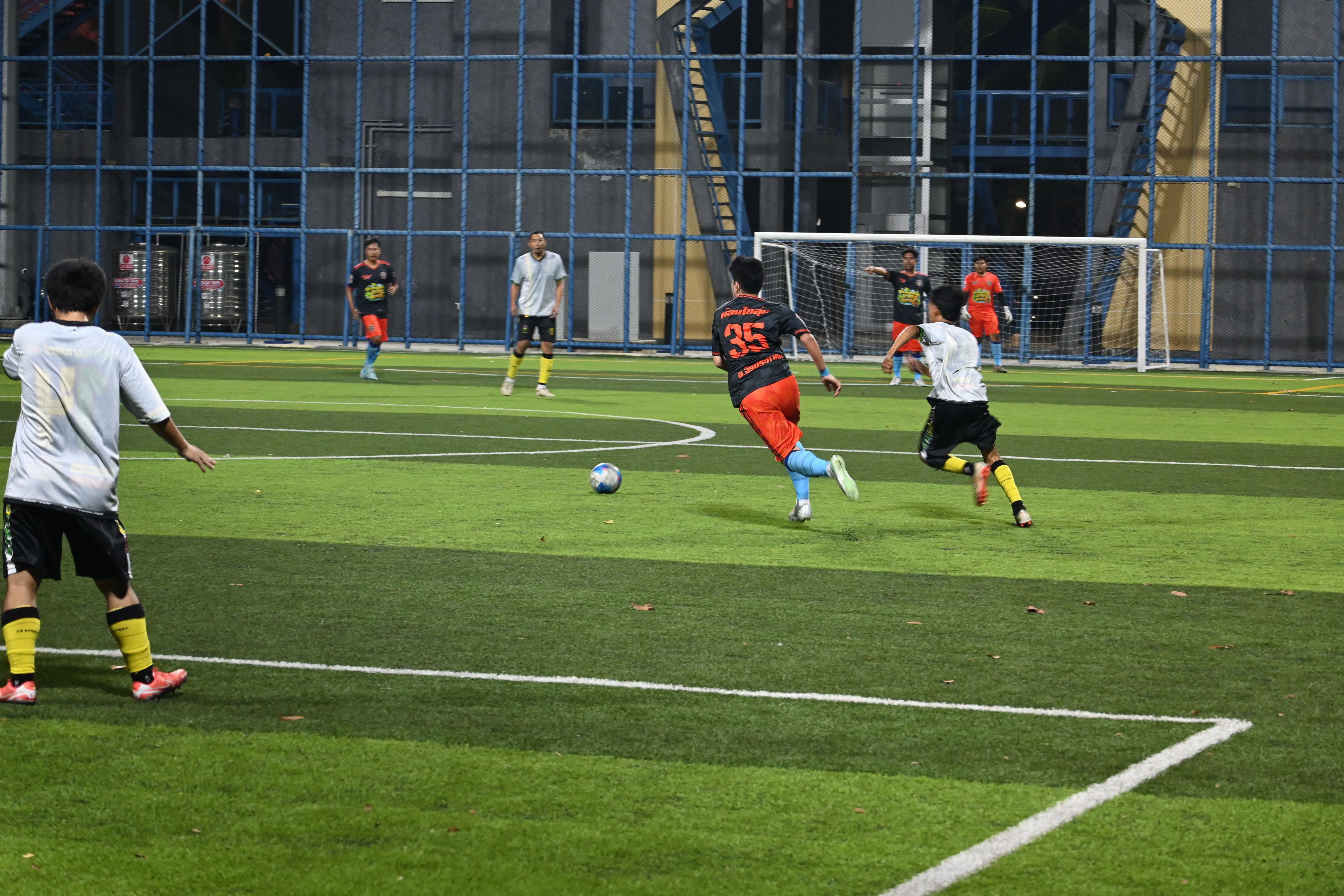 Soccer player in orange jersey dribbles toward goal as defenders pursue on a turf field.