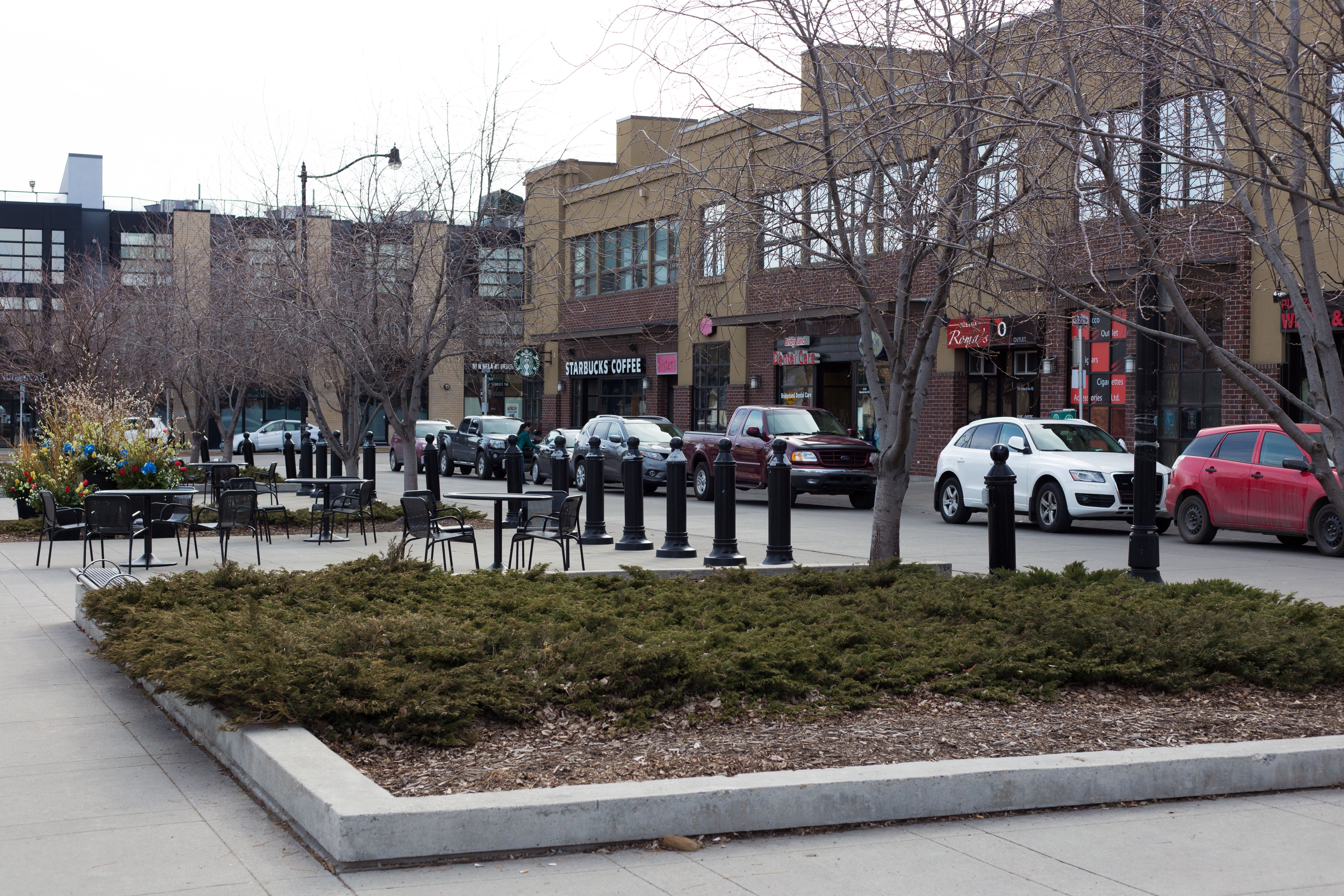 Brick commercial plaza with retail storefronts, outdoor seating, and bare trees.