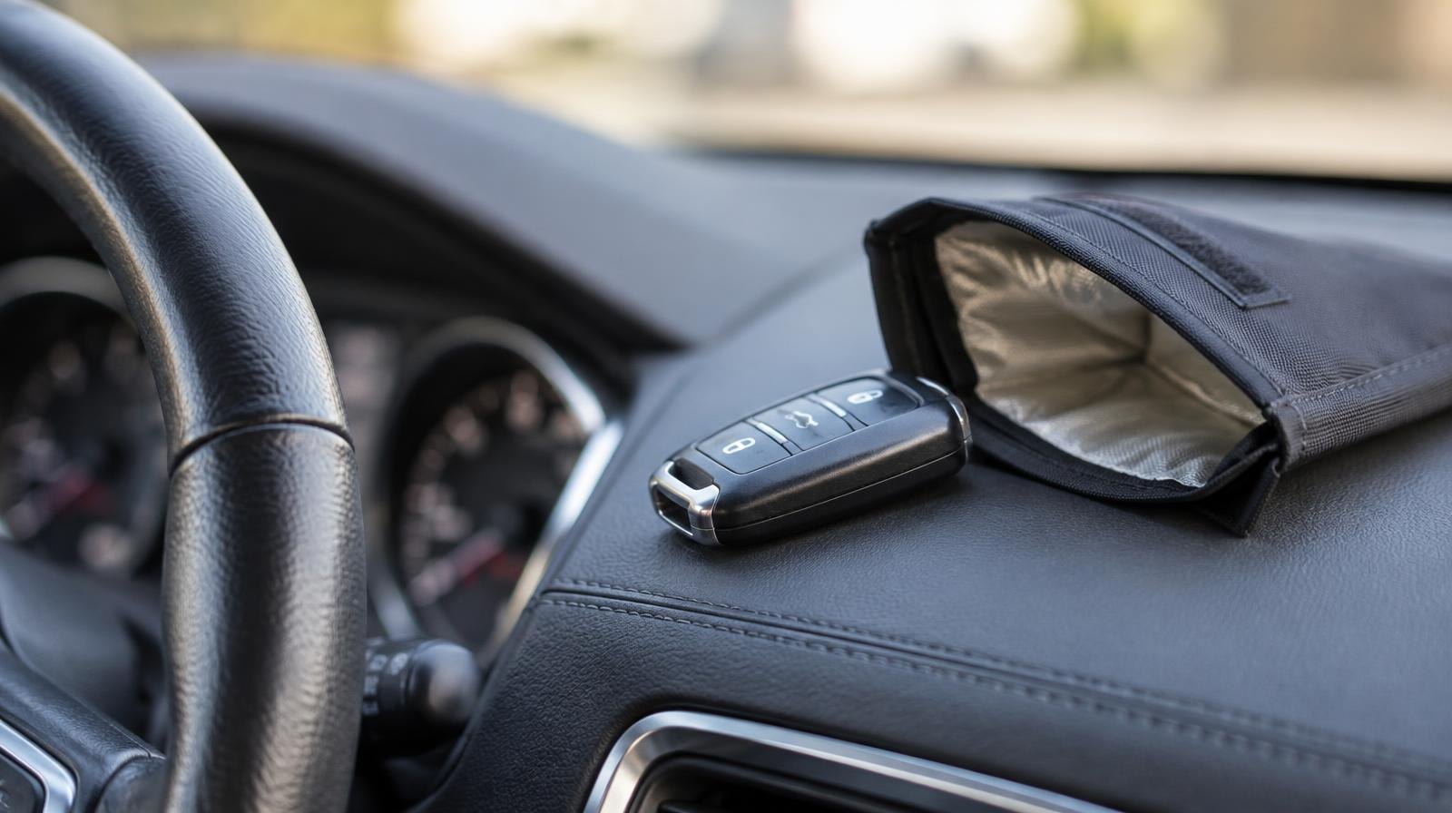 A car key fob on a dashboard next to an open Faraday bag.