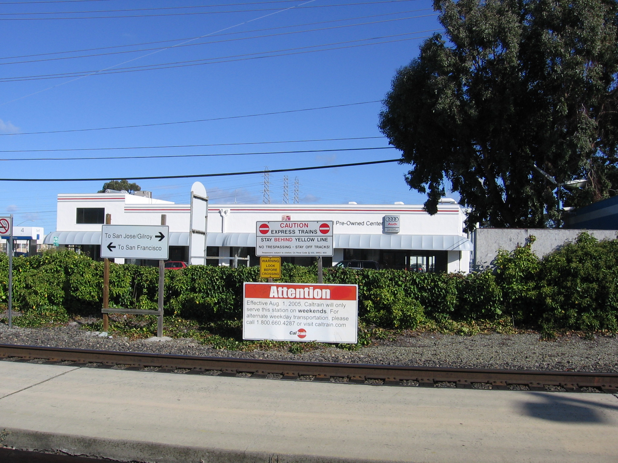 Caltrain station building with railroad tracks and directional signs in the foreground.