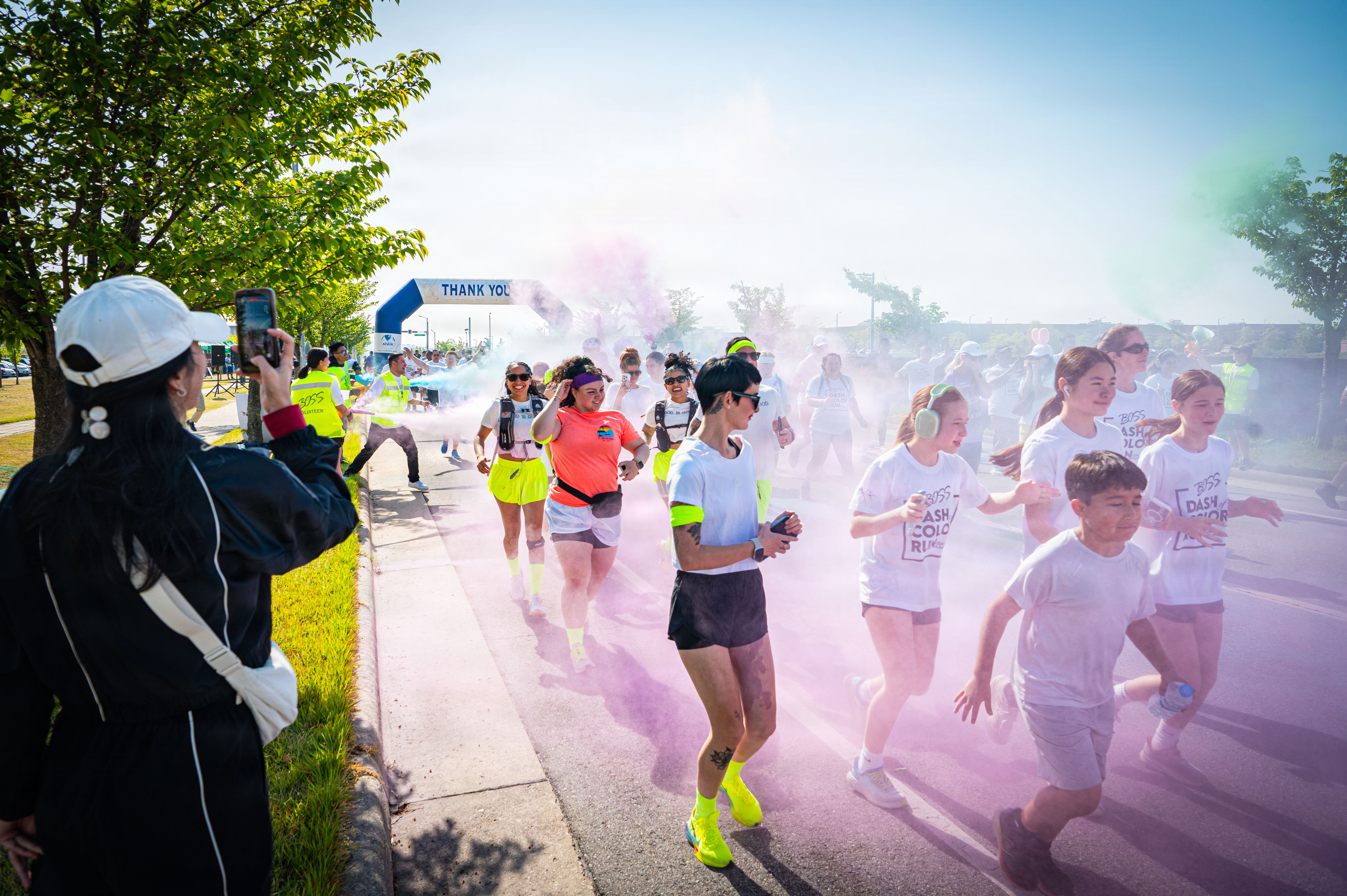 Adults and children in white shirts run through a pink powder cloud at a color run.
