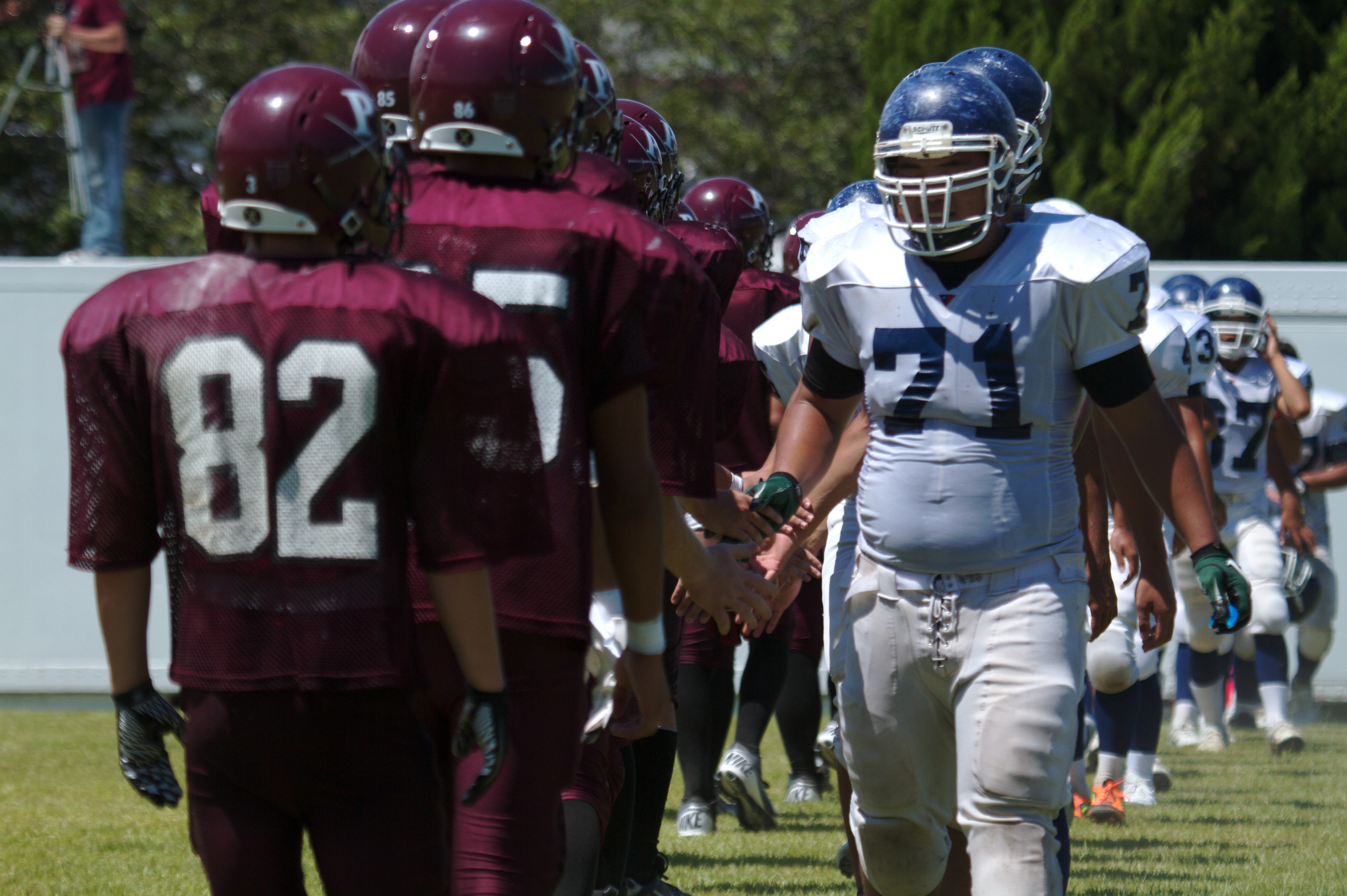 Football players from two teams shake hands on a grass field after a game.