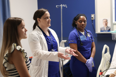 Three women, including two healthcare professionals in scrubs, tour a clinical training room at Chamberlain University’s Cincinnati campus.