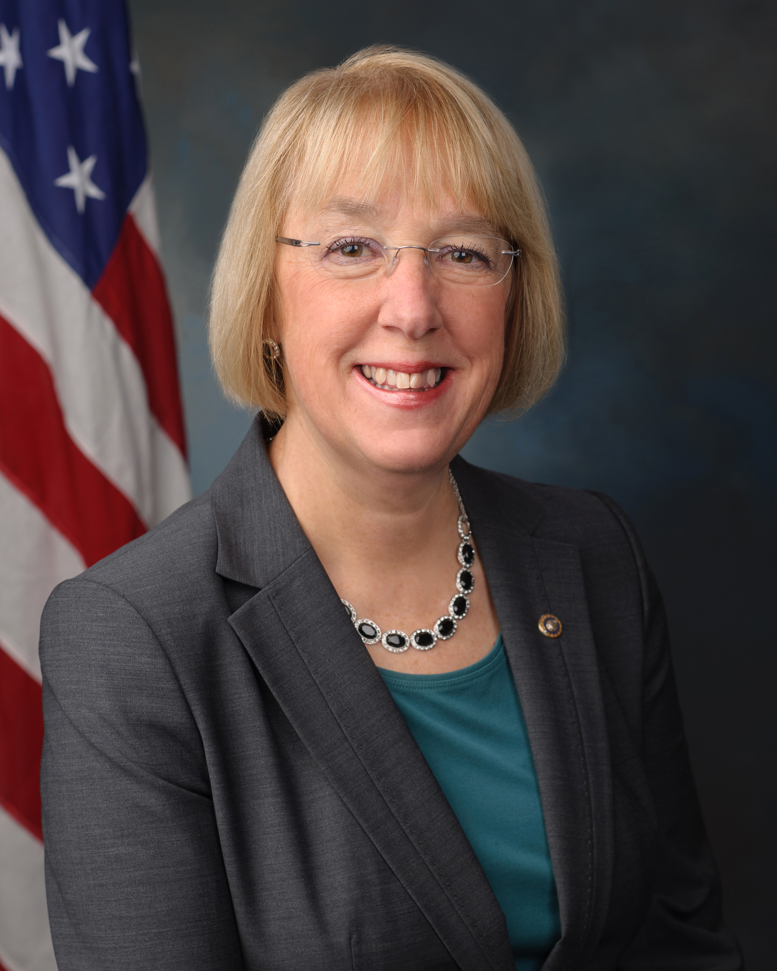 Official portrait of a woman in a gray blazer before a U.S. flag.