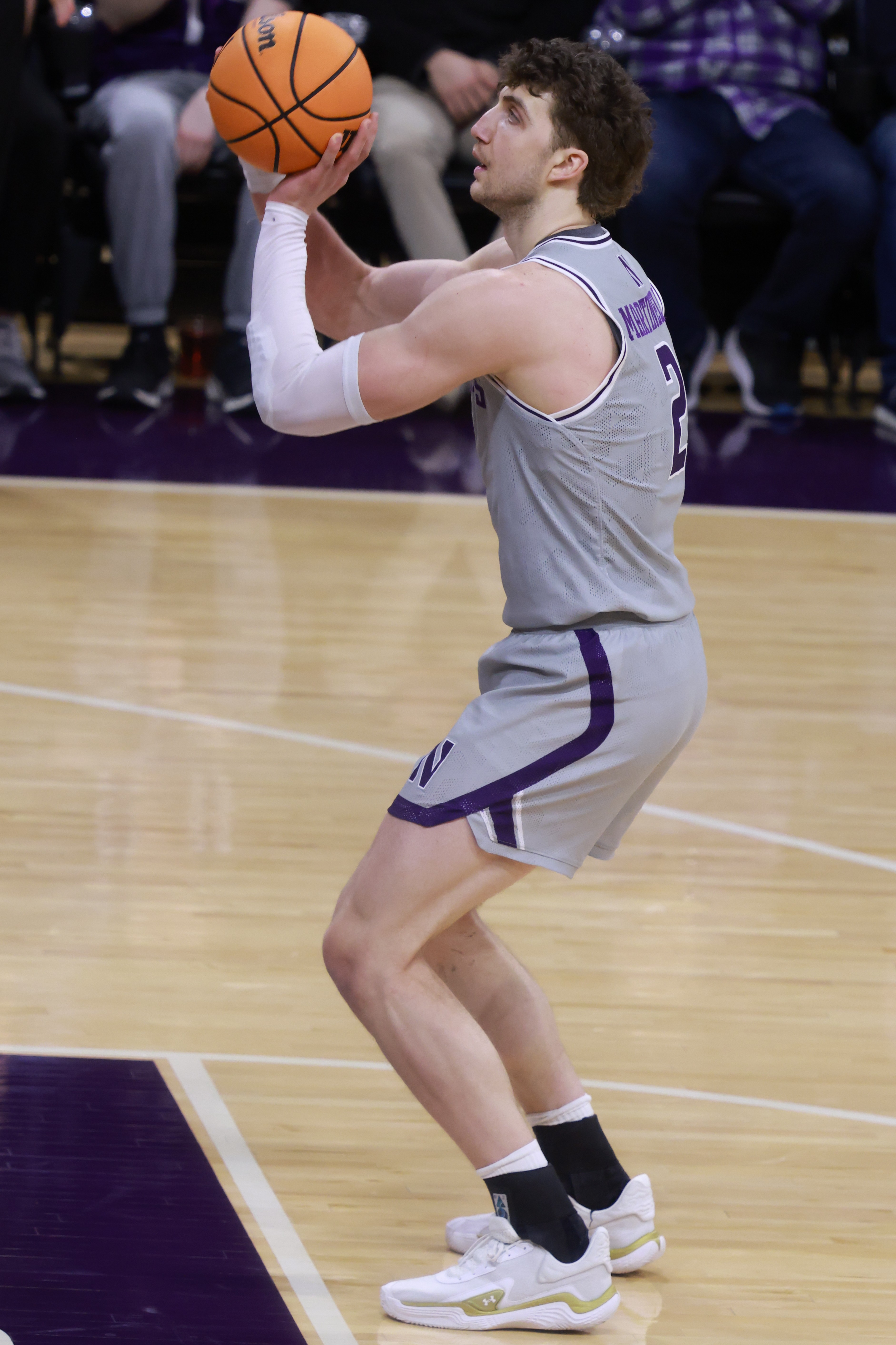 Northwestern basketball player in gray uniform holds ball in shooting stance on court.