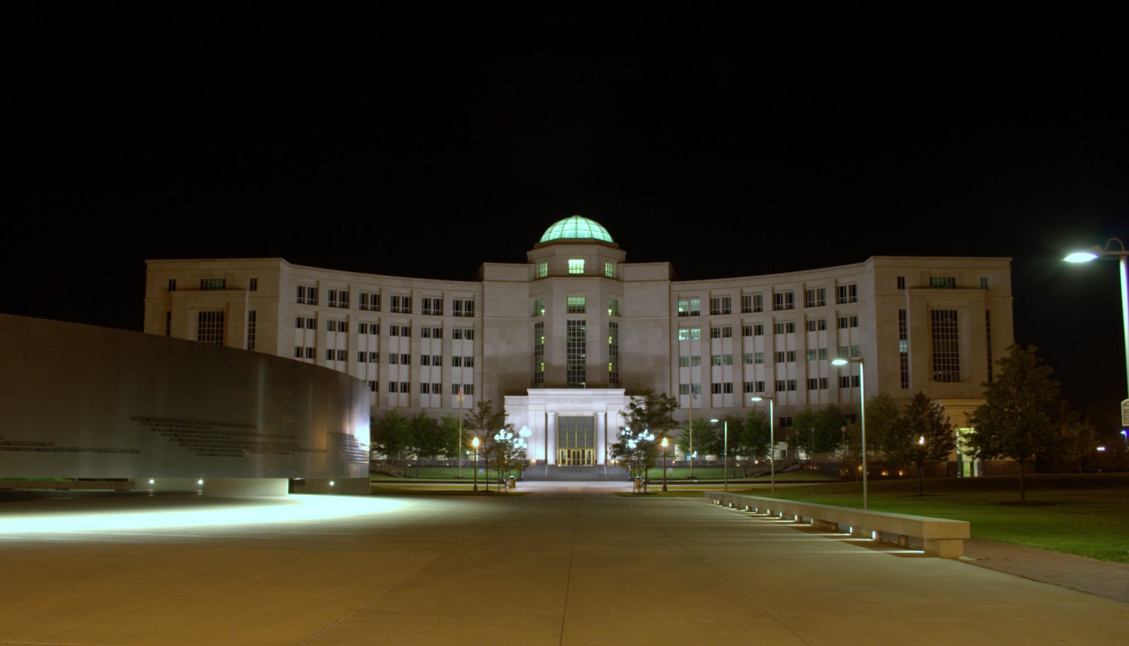 Government building with illuminated green dome at night, wide plaza in foreground.
