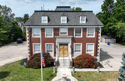 Two-story red brick colonial-style building with dormer windows and an American flag out front.