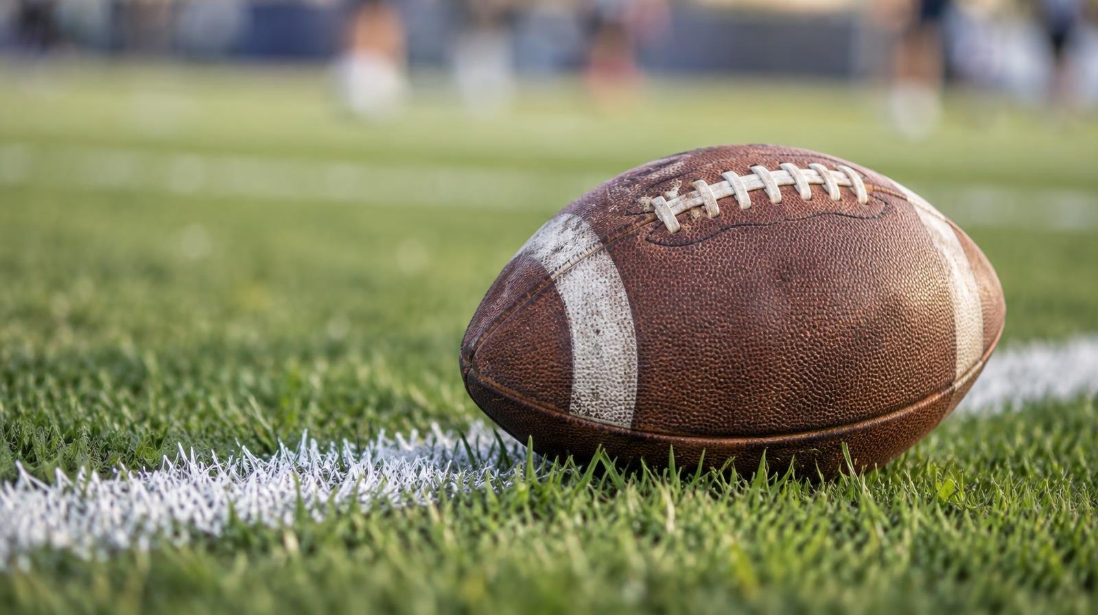 An American football resting on green grass beside a white yard line.