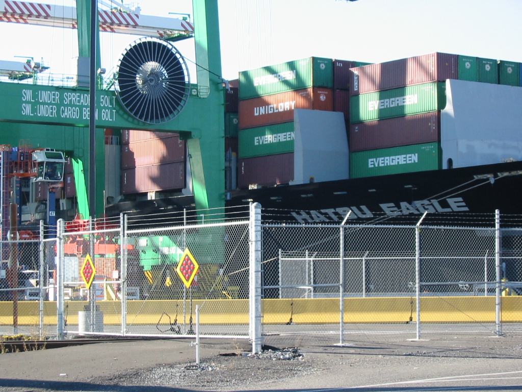 Large green gantry crane towers over stacked shipping containers at a port terminal.