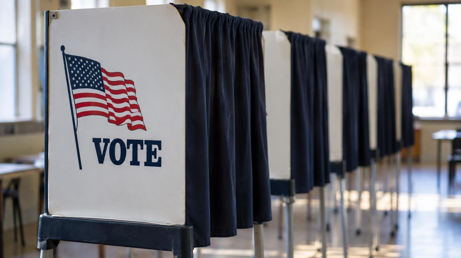 A row of empty voting booths with privacy curtains in a well-lit room.