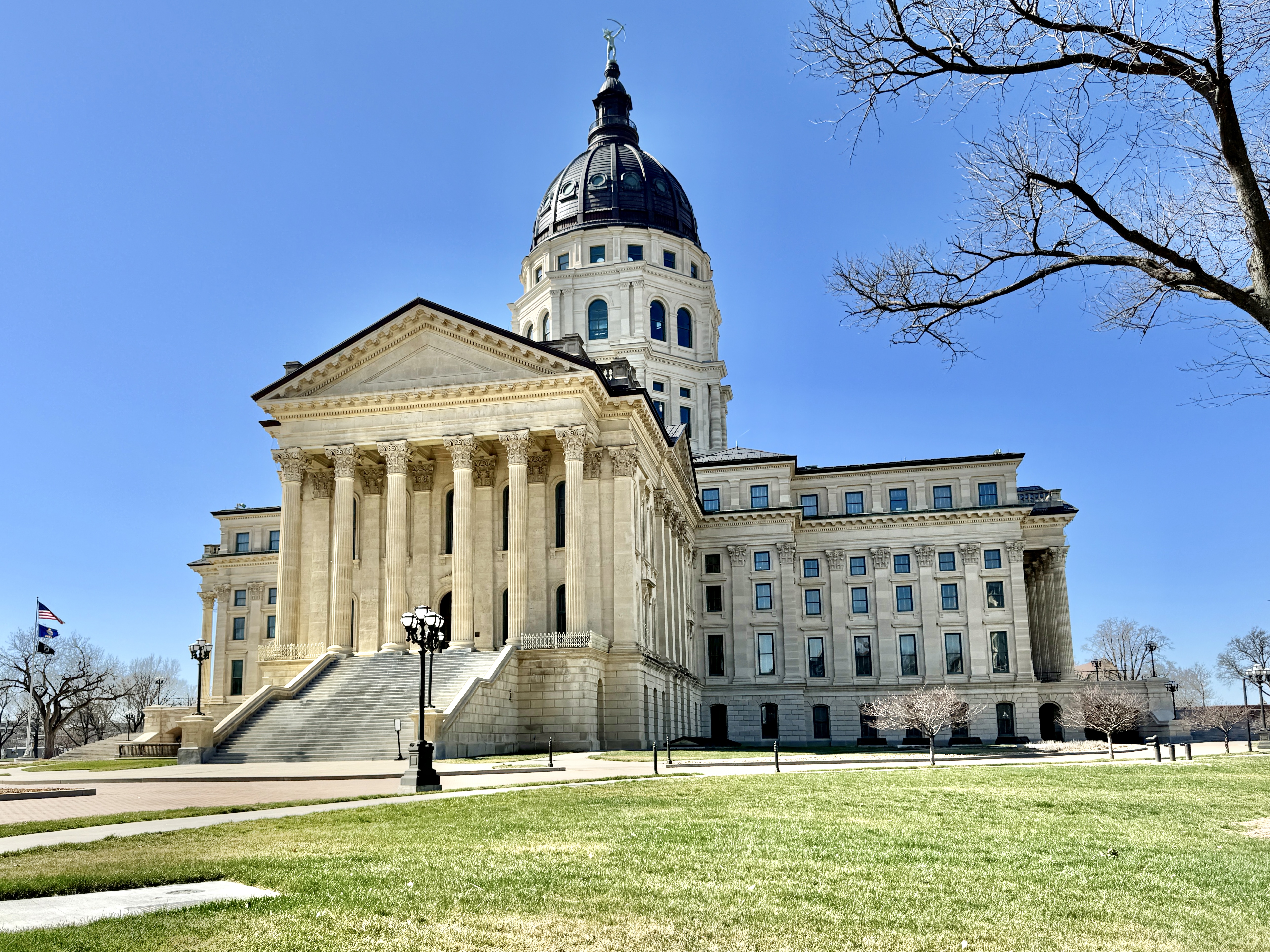 The Kansas State Capitol building with its large dome and classical columns under a clear blue sky.