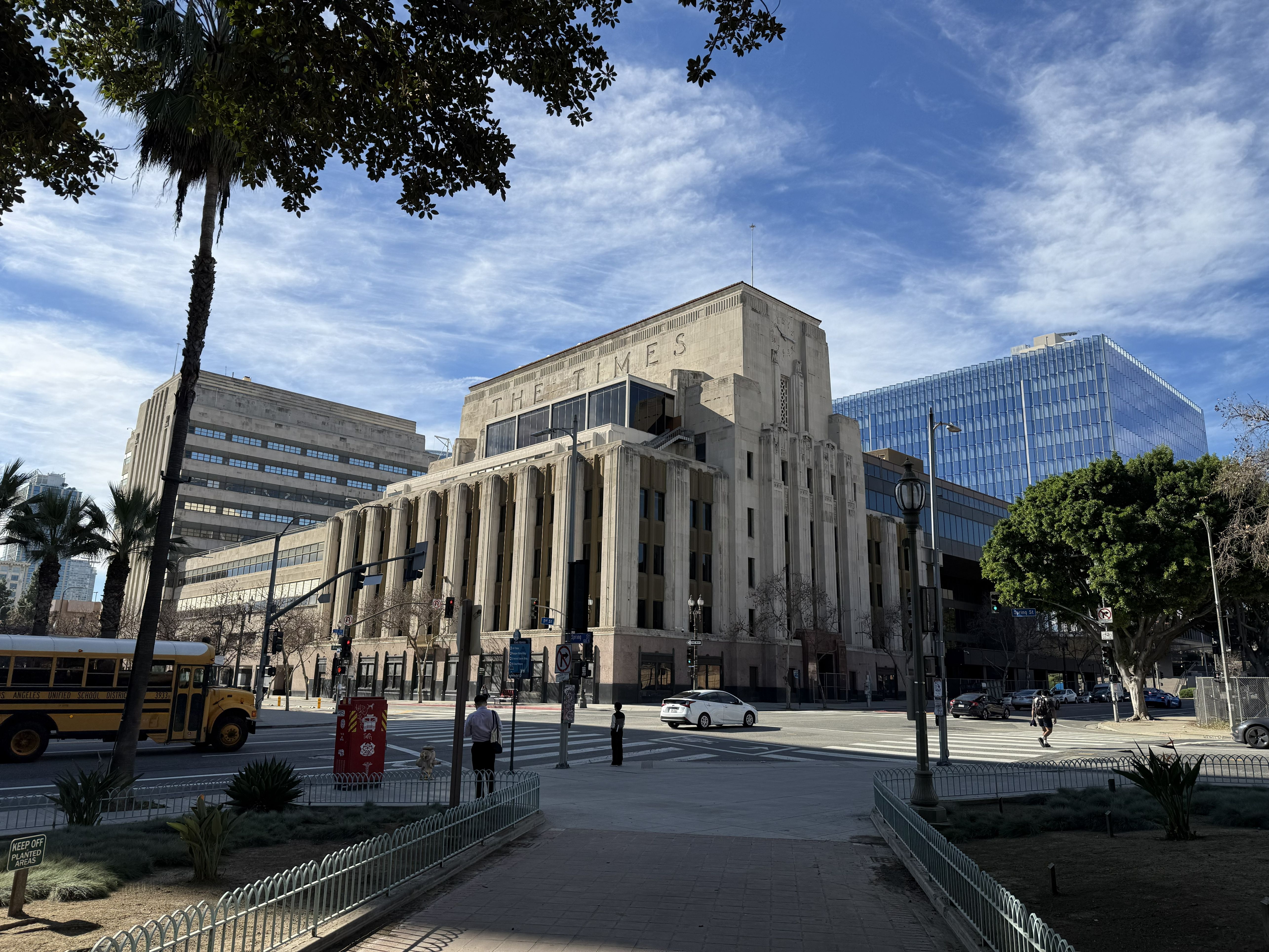 Art Deco building at a downtown Los Angeles intersection with palm trees and a school bus.