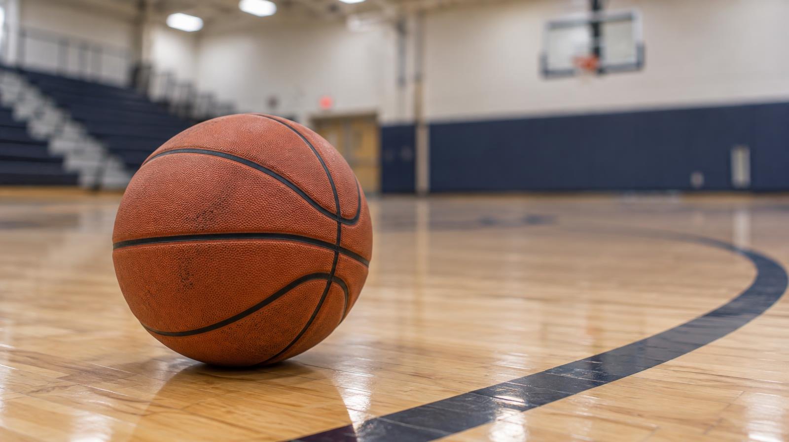 A basketball sitting on a hardwood gym floor near a painted court line.