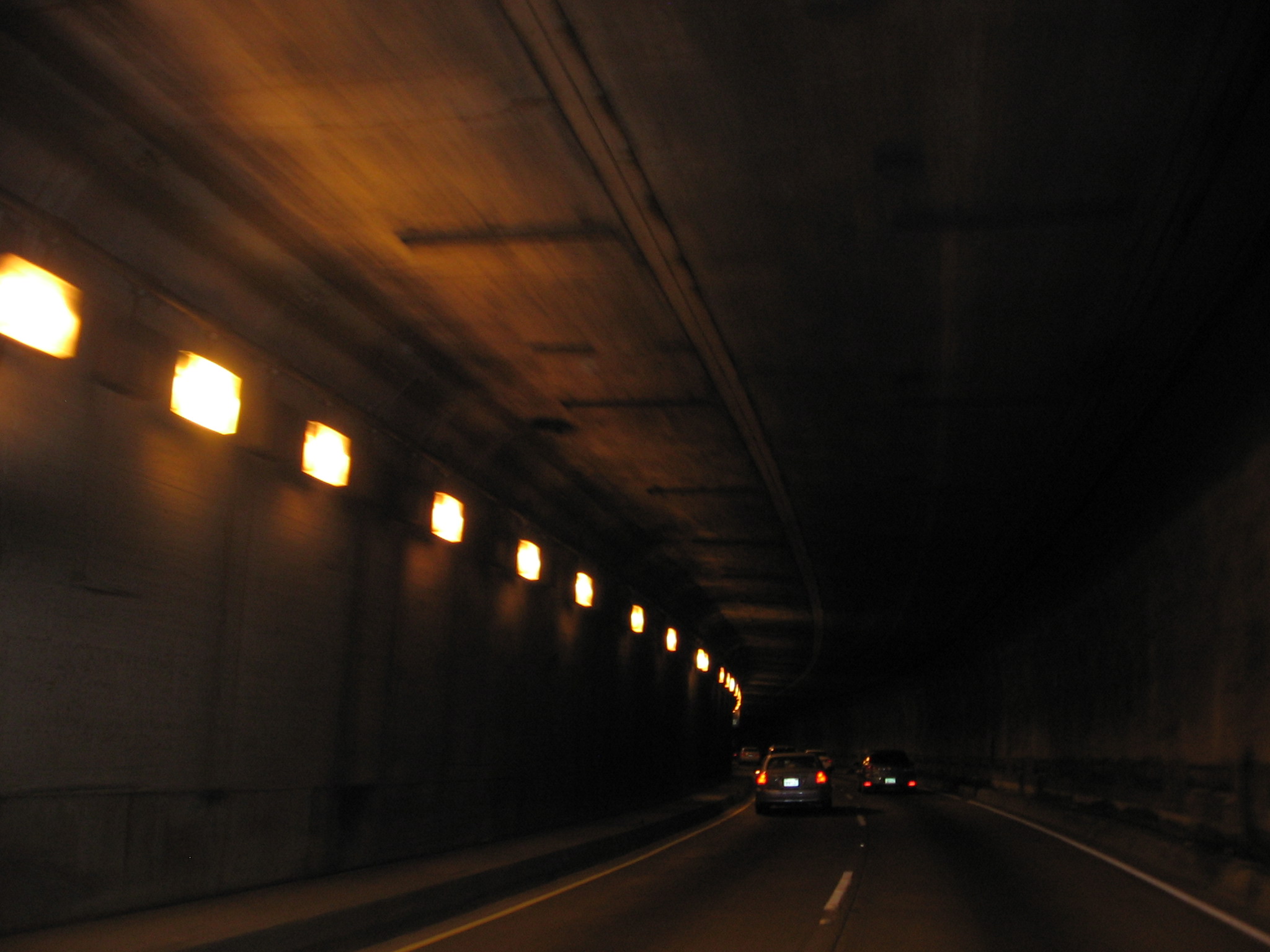 Inside a road tunnel with wall-mounted square lights and a car ahead.