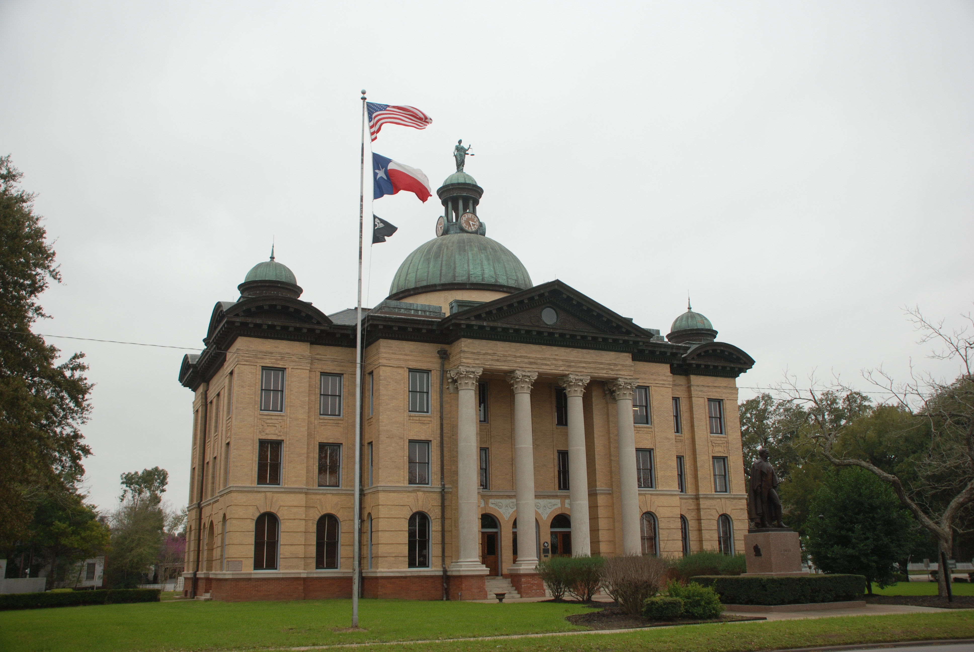 Neoclassical brick courthouse with green copper dome and US and Texas flags on flagpoles.