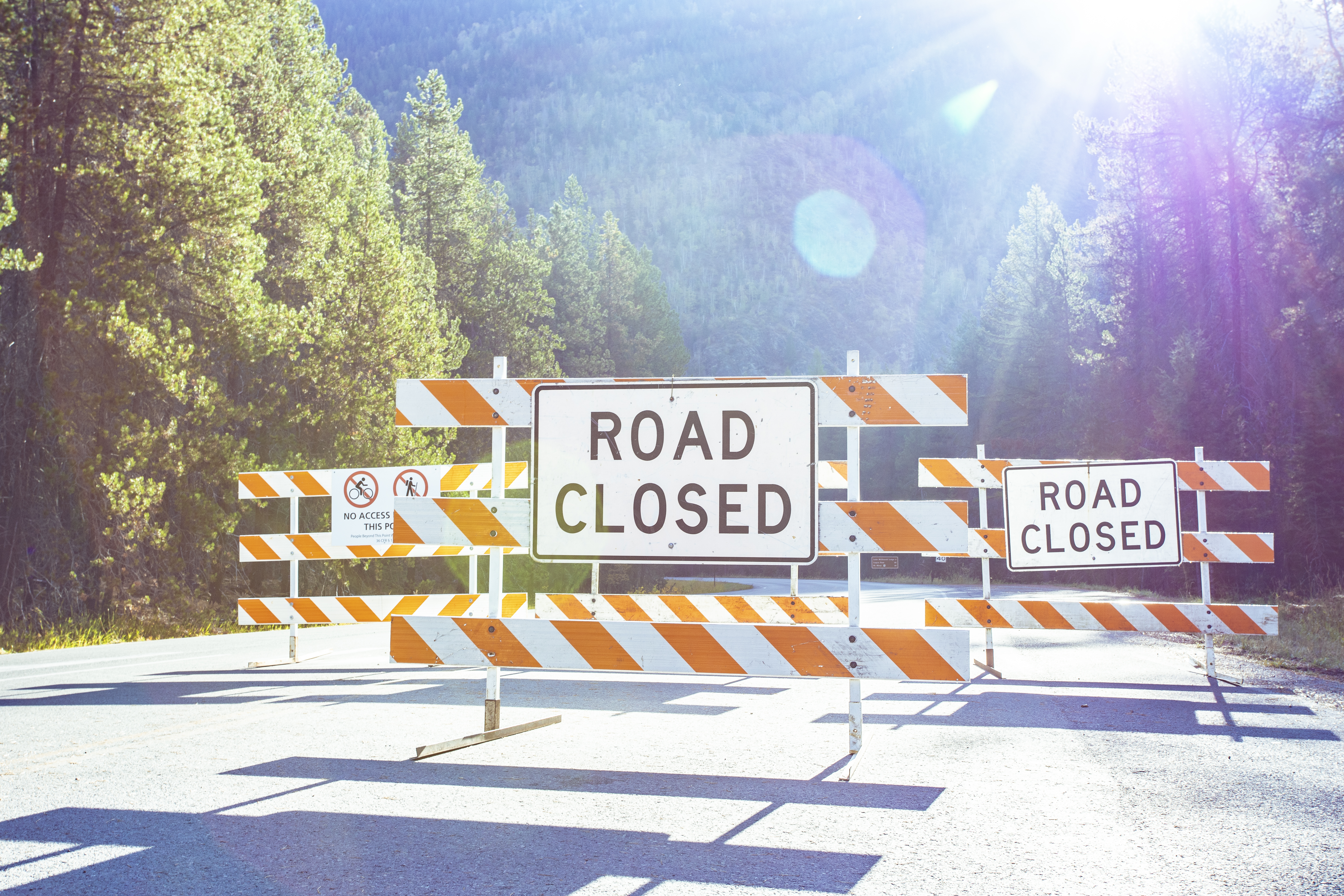 Two orange-and-white barricades with Road Closed signs block a paved road.