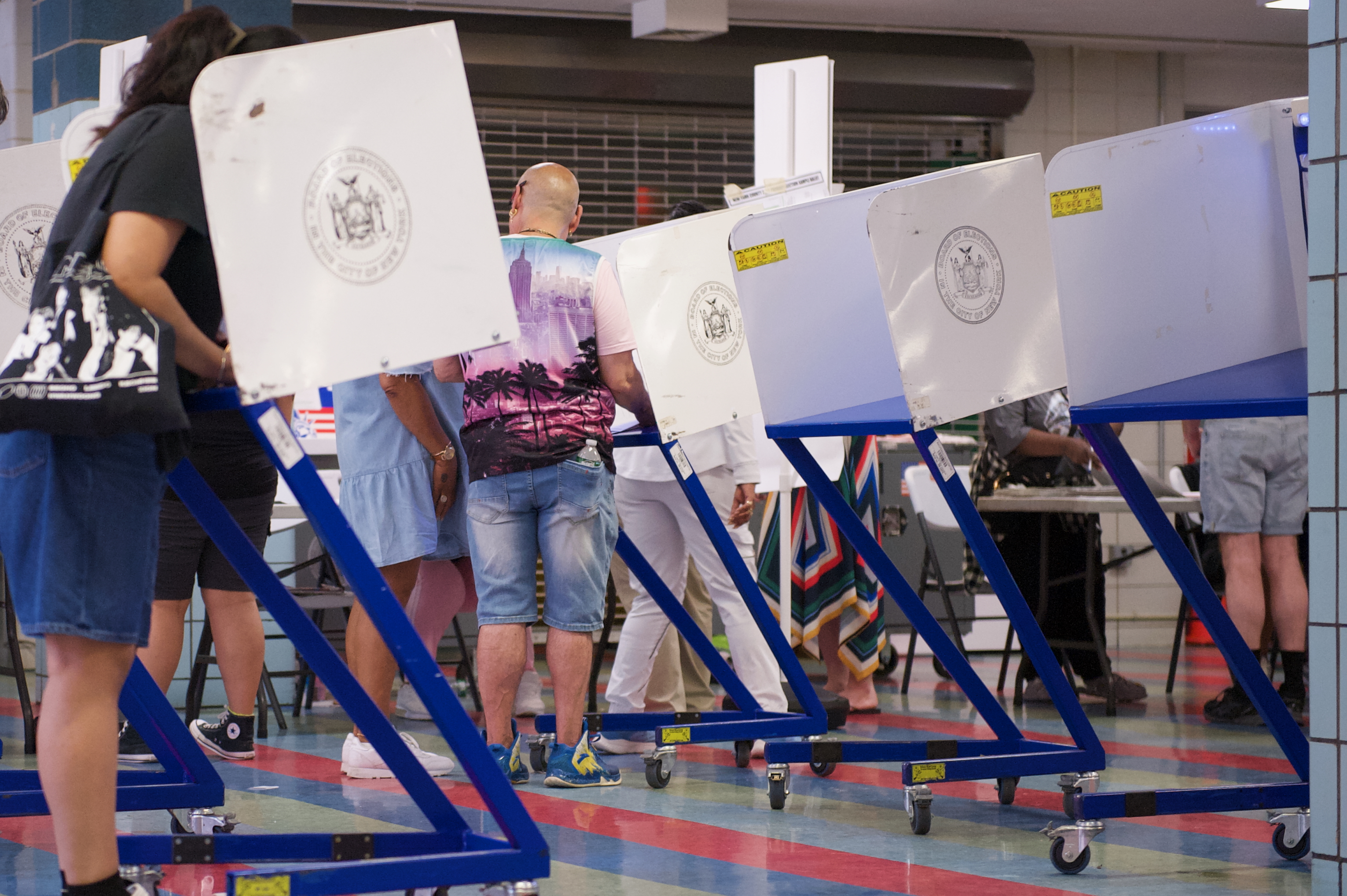 Several voters stand at white privacy voting booths inside a large polling location.