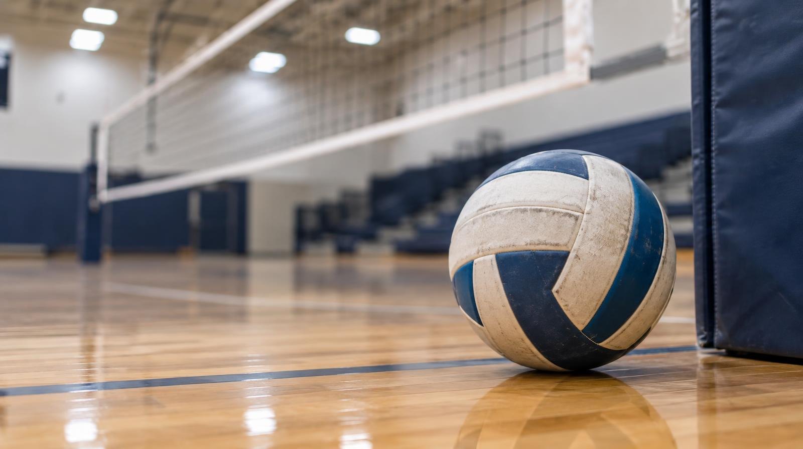 A volleyball resting on a hardwood gymnasium floor near a net post.