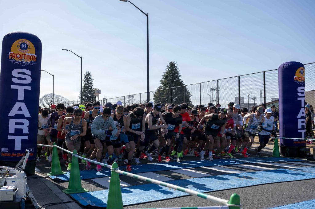 A crowd of runners waits at the starting line of an outdoor race.