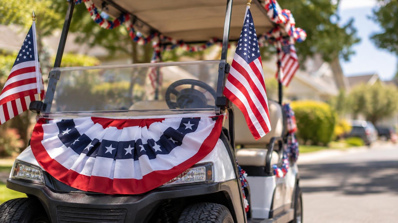 A golf cart decorated with patriotic bunting and small American flags on a sunny street.