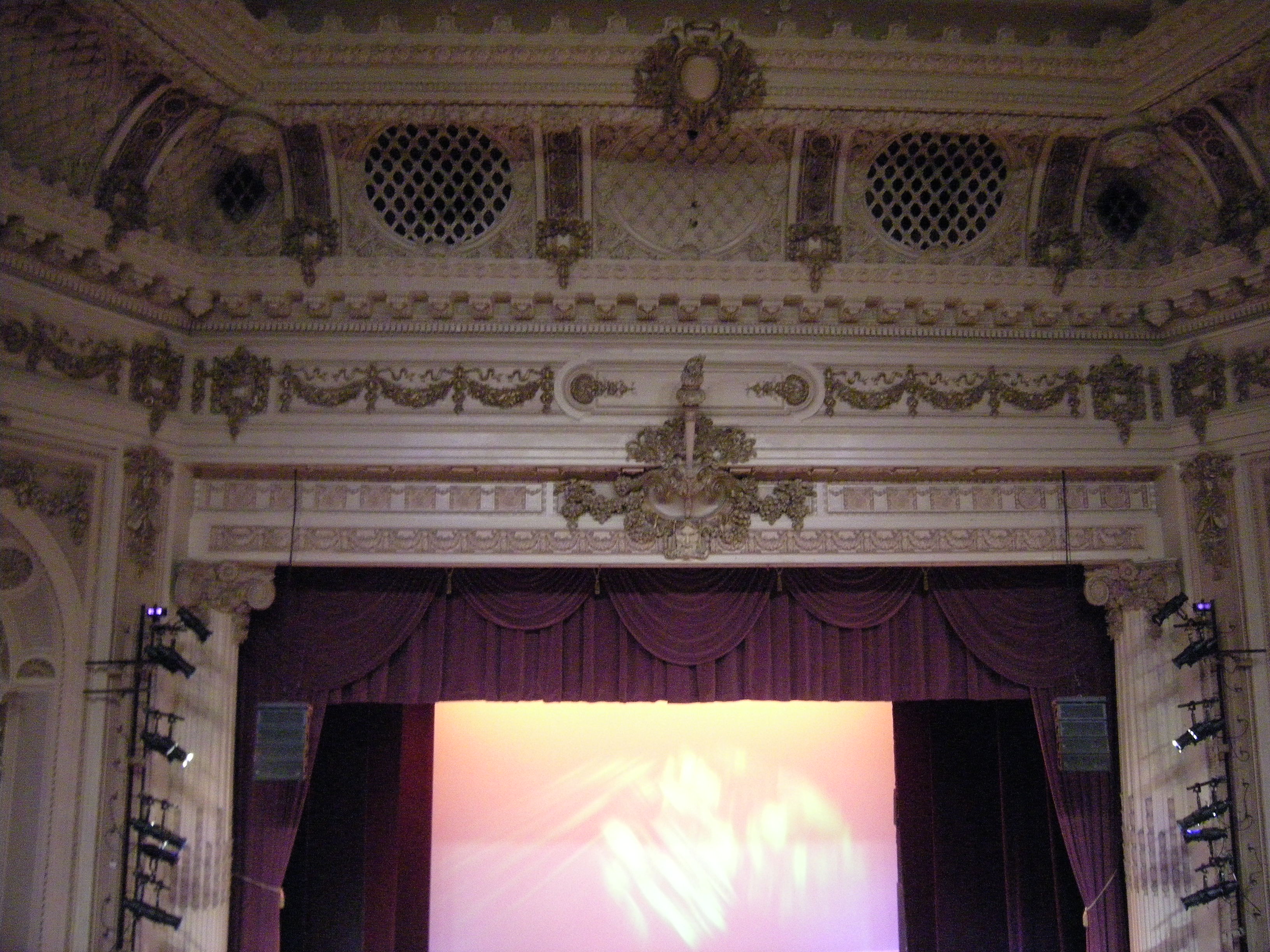 Ornate theater interior with elaborate plasterwork proscenium arch and deep red stage curtain.
