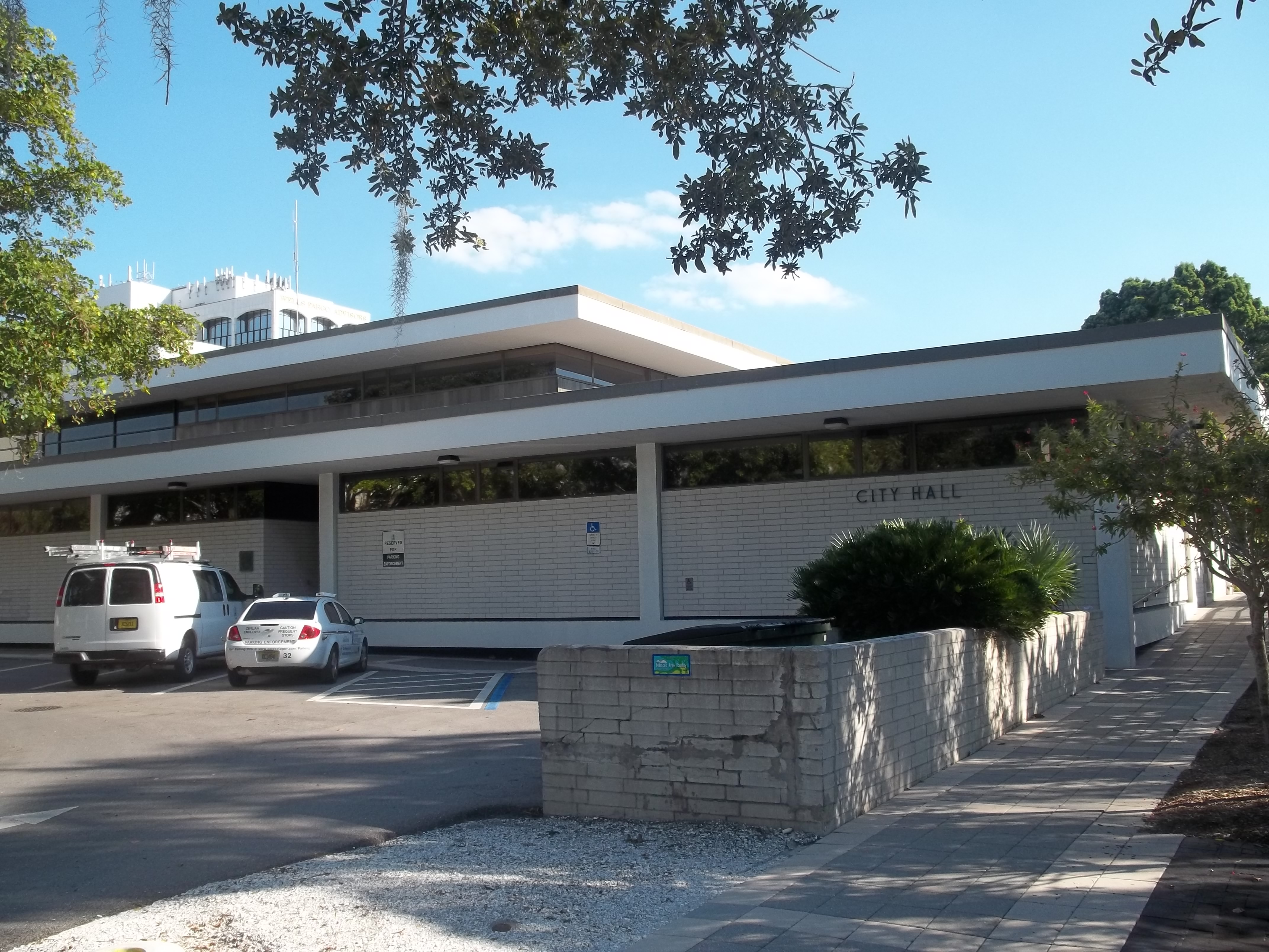 Mid-century modern brick building with City Hall signage and parked cars out front.