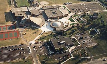 Aerial view of a large school campus with buildings, parking lots, and athletic courts.