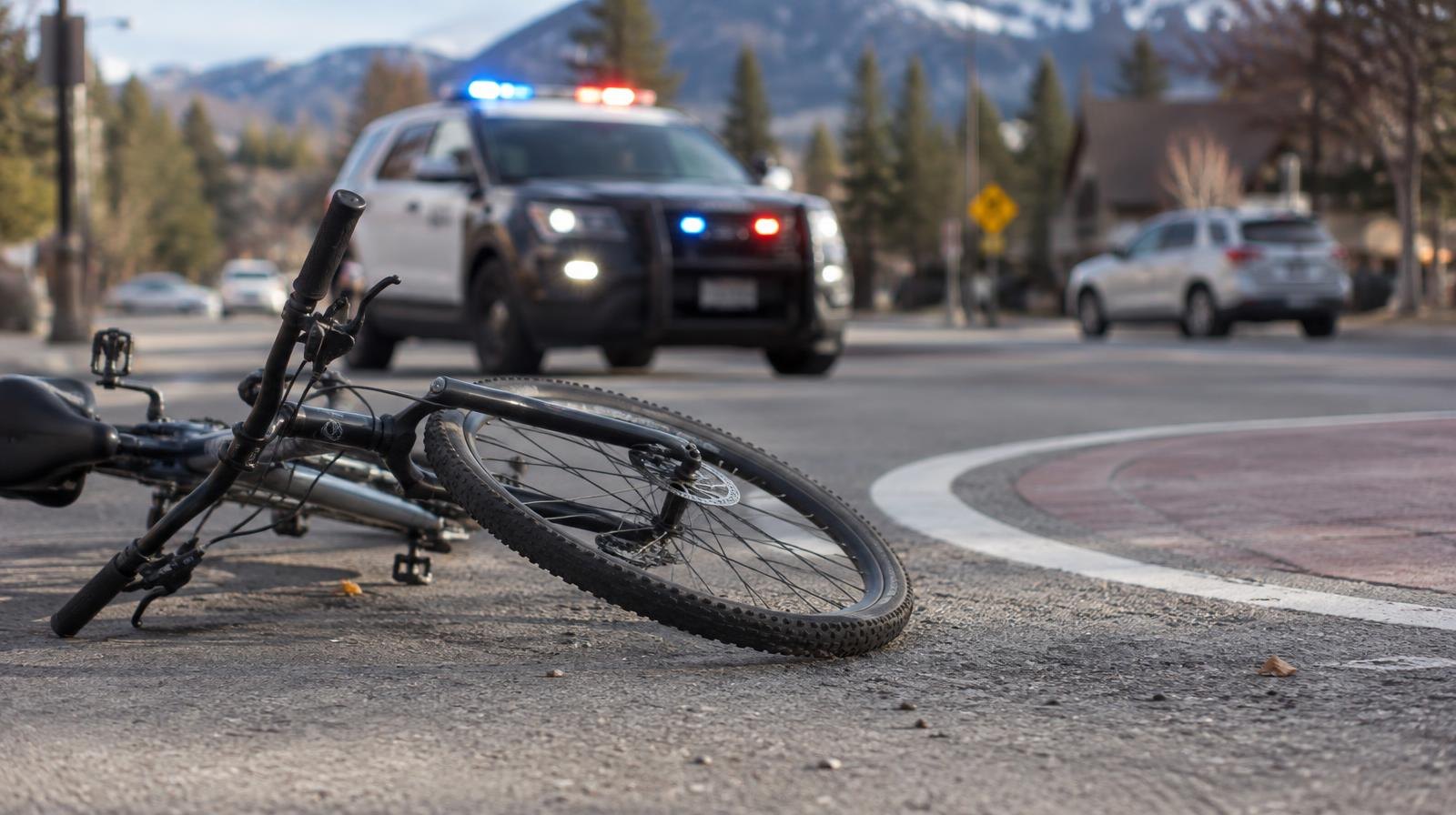 A bicycle on its side near a roundabout marking with police lights in the background.