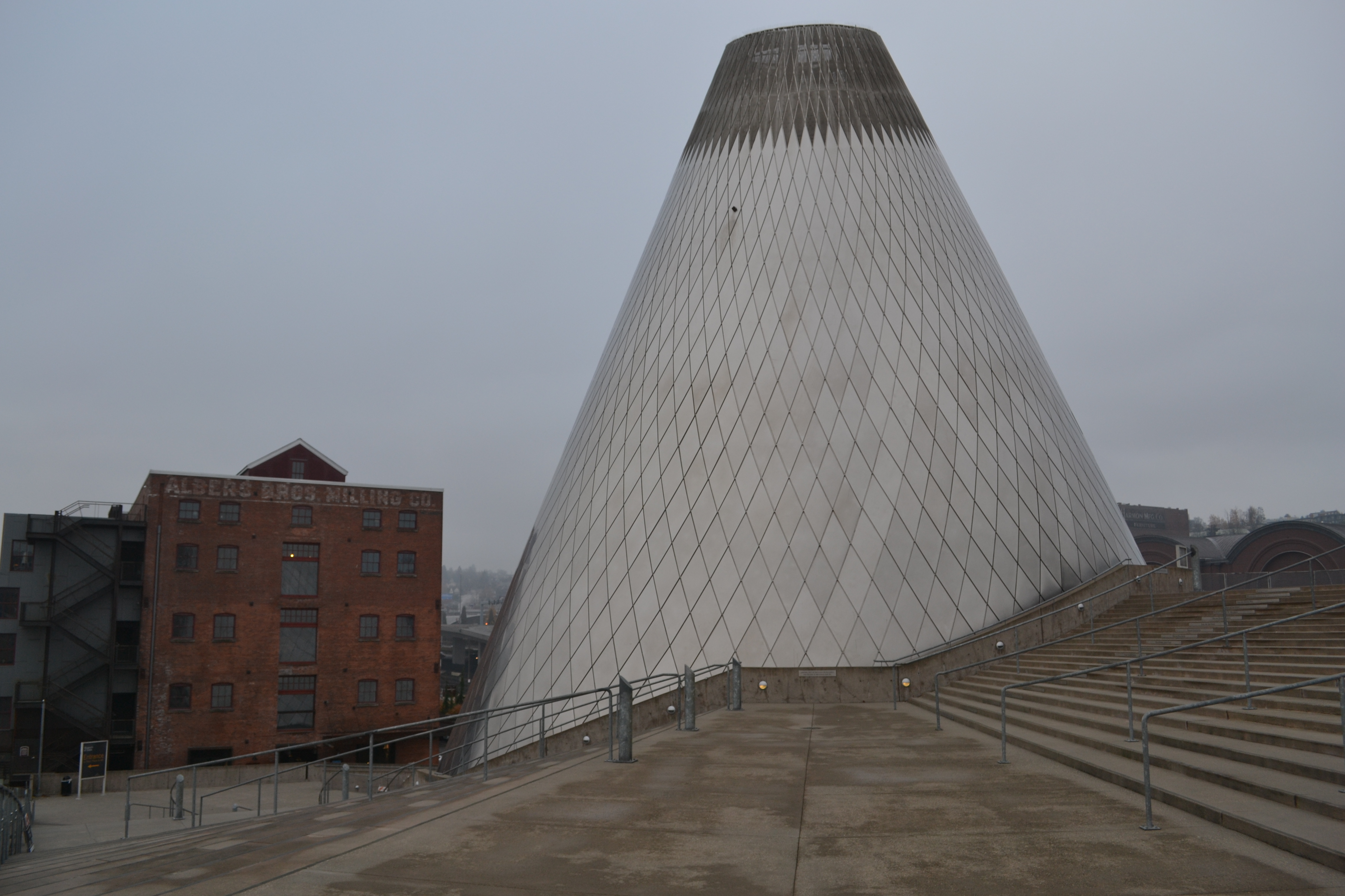 Cone-shaped Museum of Glass exterior with entrance stairs on an overcast day.