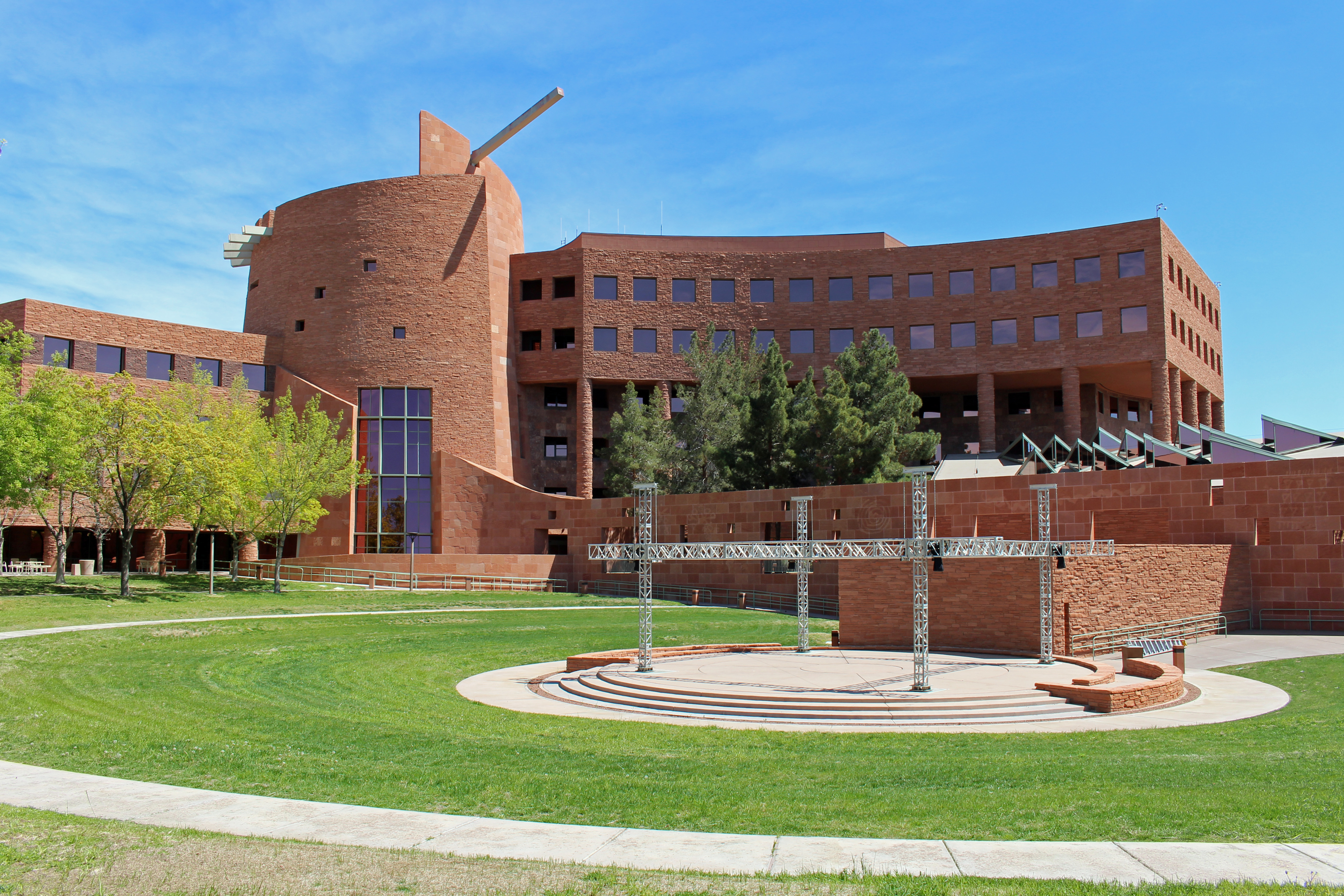 Curved red-brick government building with an outdoor amphitheater and green lawn.