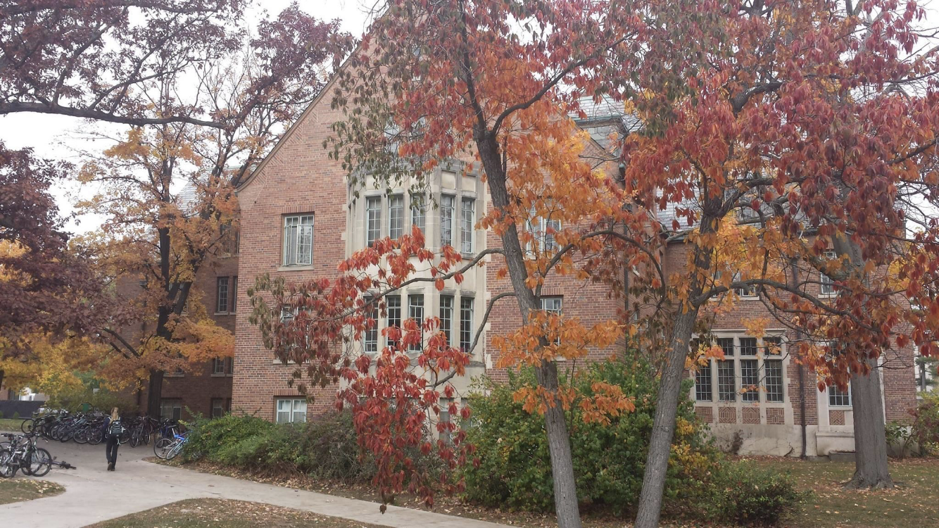 Brick campus building surrounded by trees with red and orange autumn leaves.