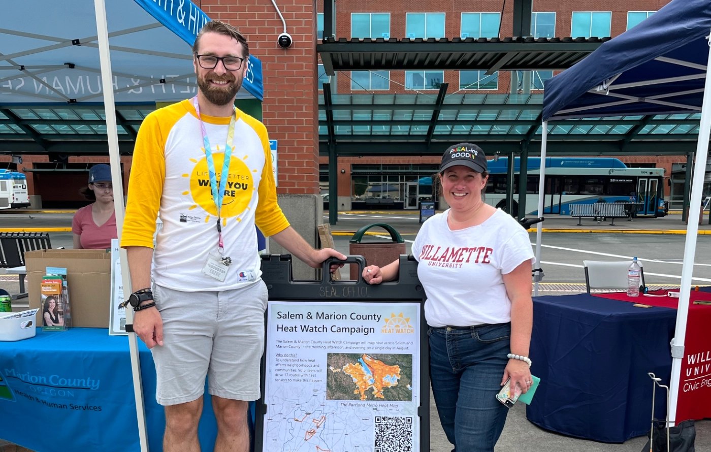 Two people smile at an outdoor event booth labeled Salem and Marion County Heat Watch Campaign.