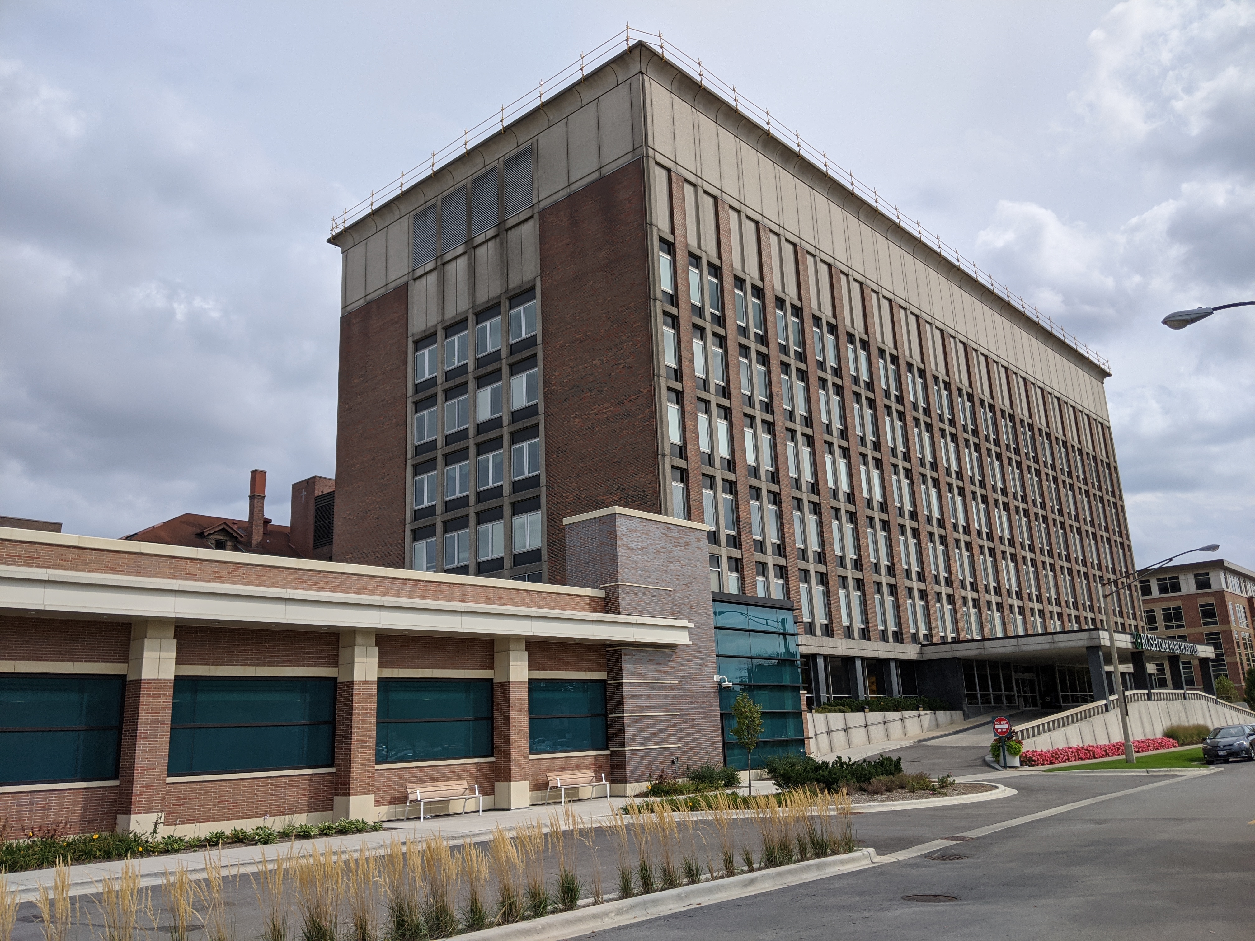 Multi-story brick and glass hospital building with a teal-paneled lower wing along a street.
