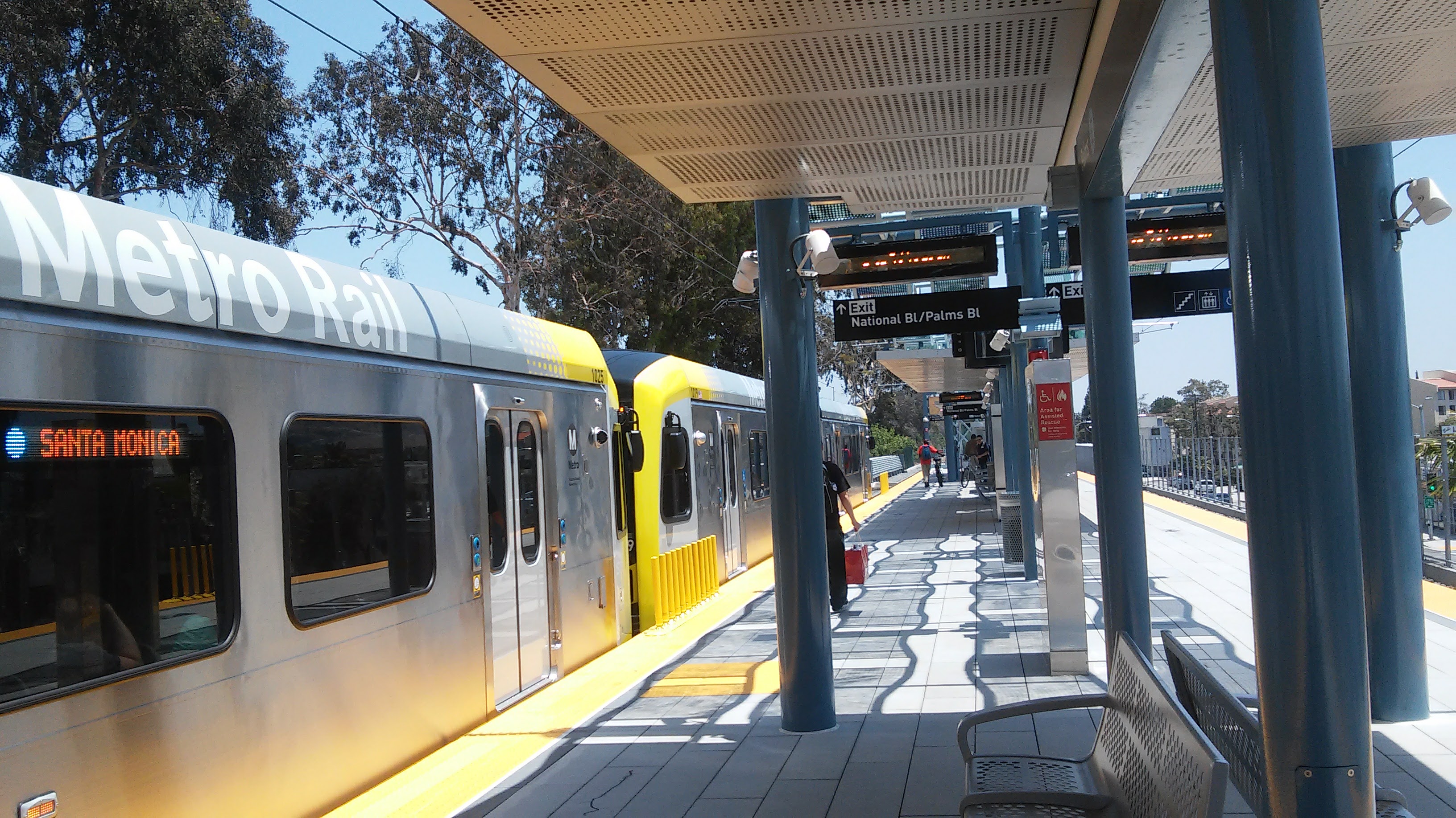 Metro Rail train stopped at a covered station platform with blue support columns.