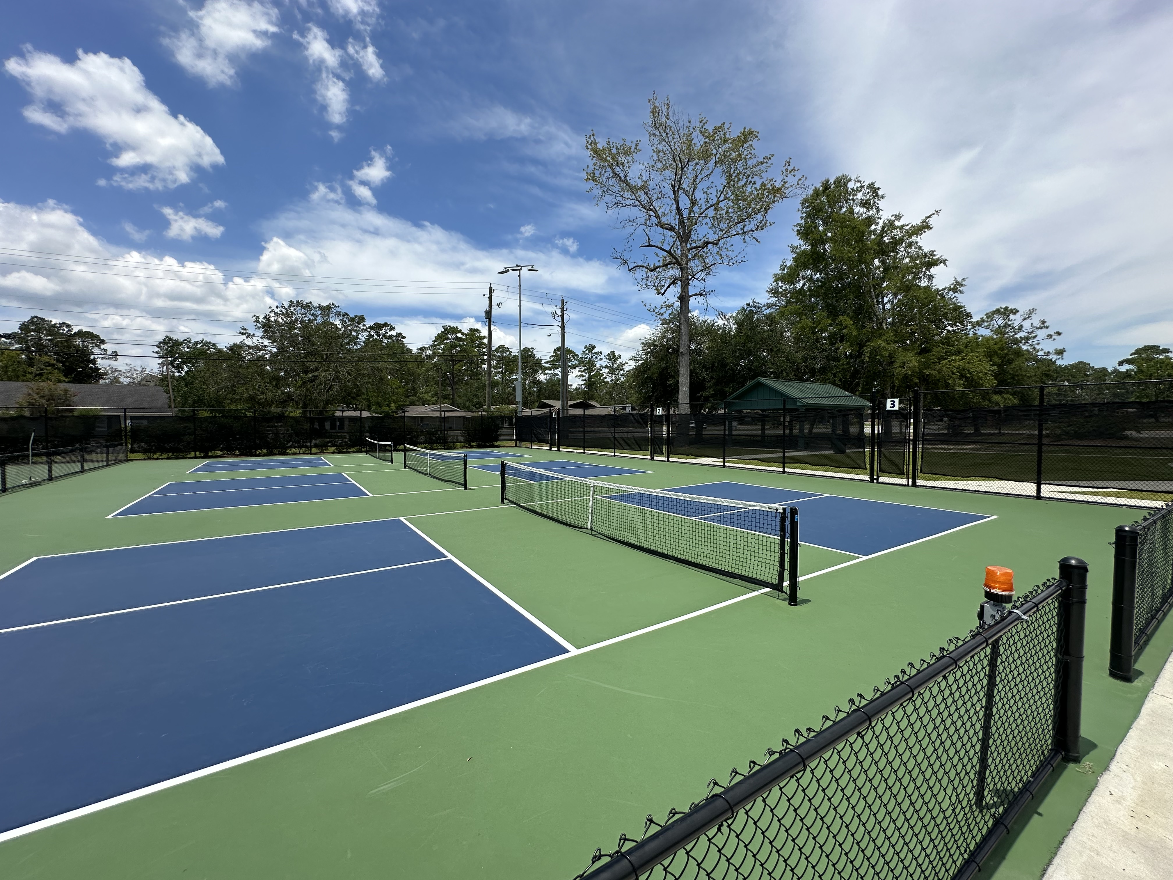 Three outdoor pickleball courts with blue and green surfaces and chain-link fencing.