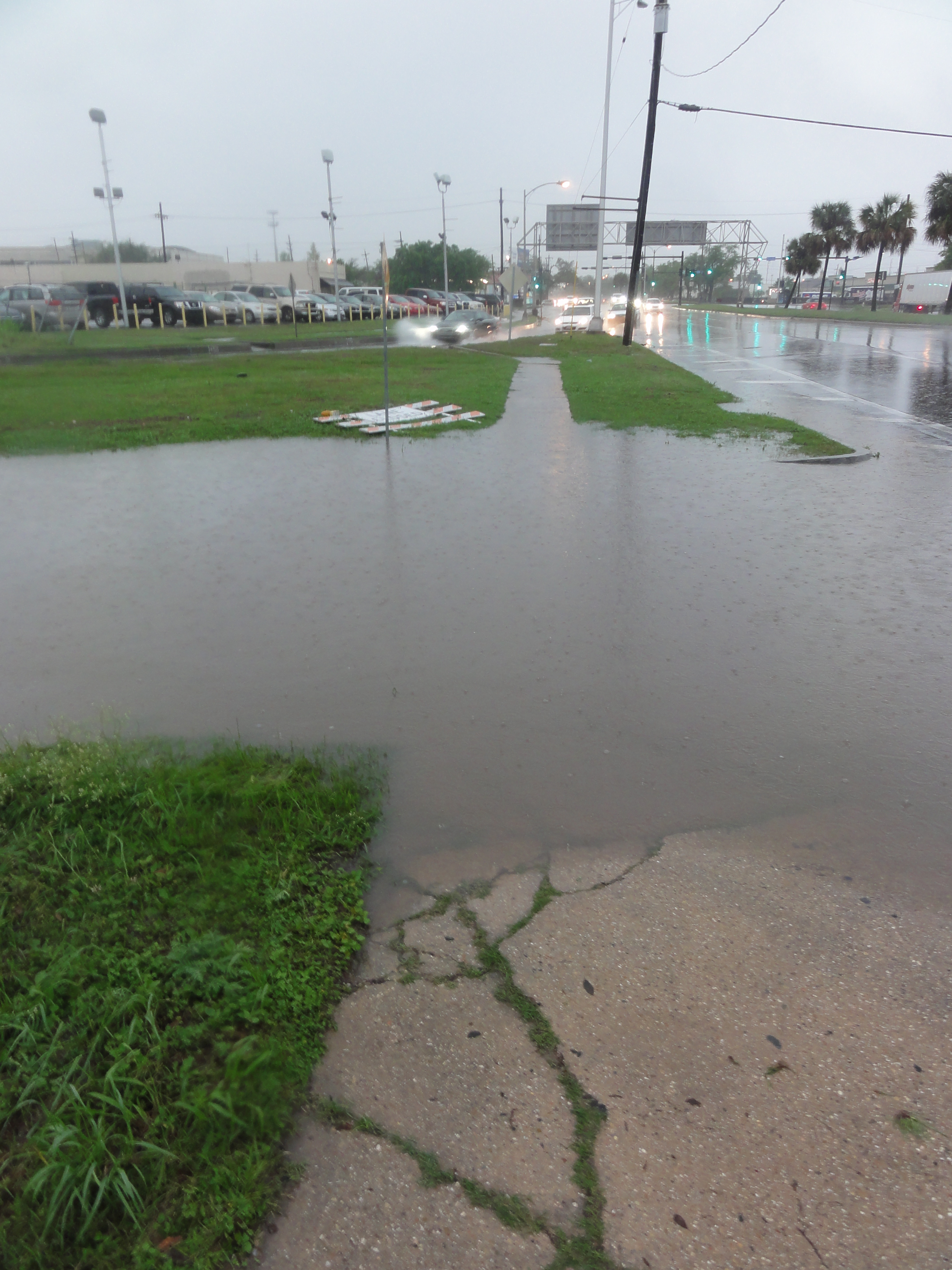 Flooded sidewalk covered in standing water along an urban street under overcast skies.