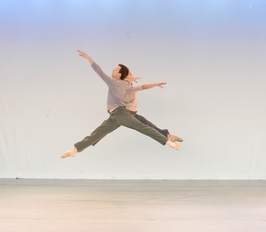 A male dancer mid-leap with arms and legs fully extended.