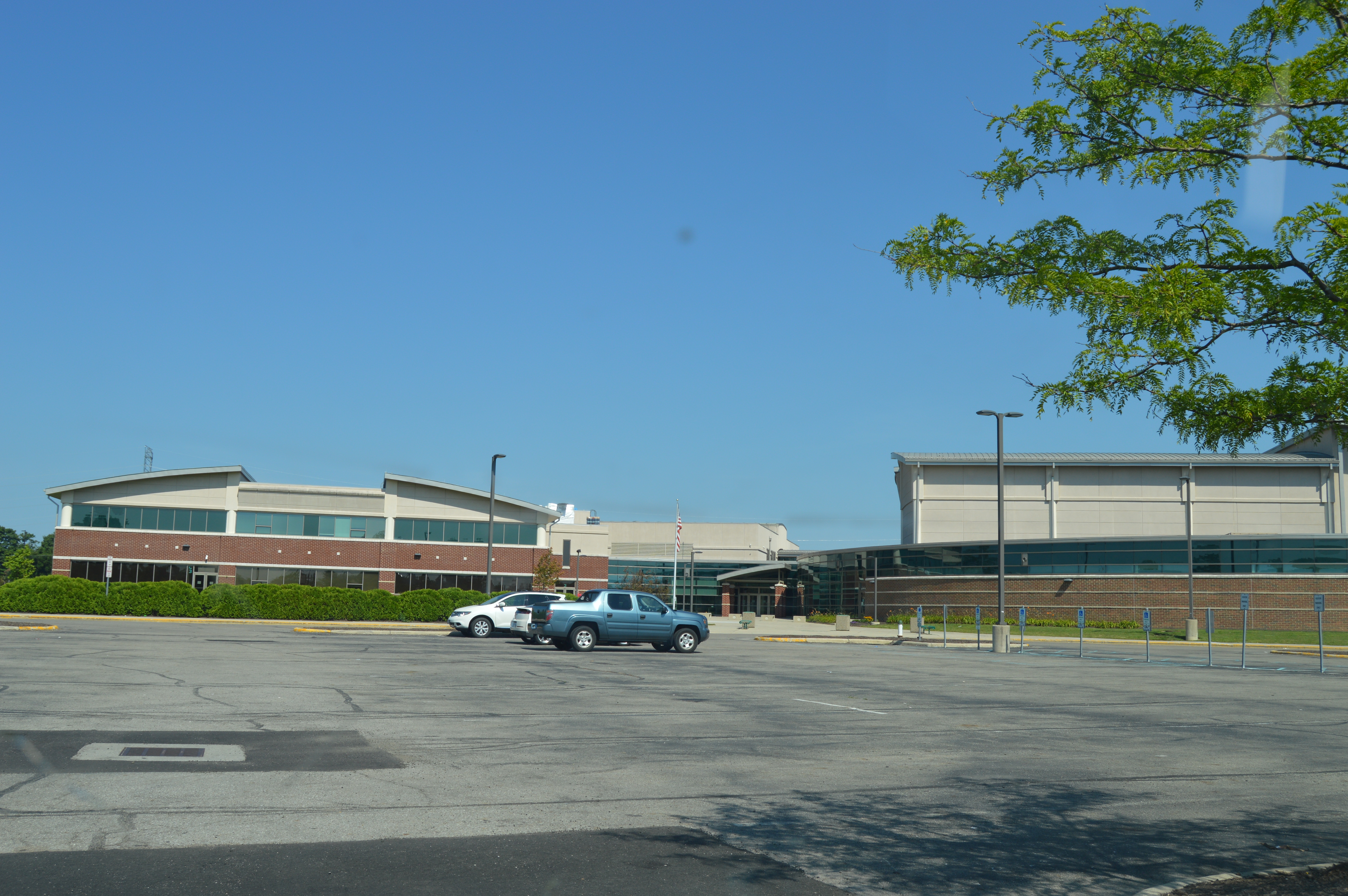 Exterior of a large brick high school building with a parking lot under a clear blue sky.