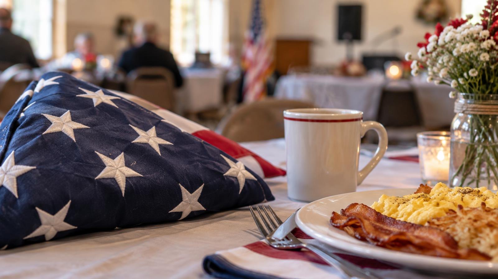 A folded American flag on a table next to a coffee mug and breakfast plate.