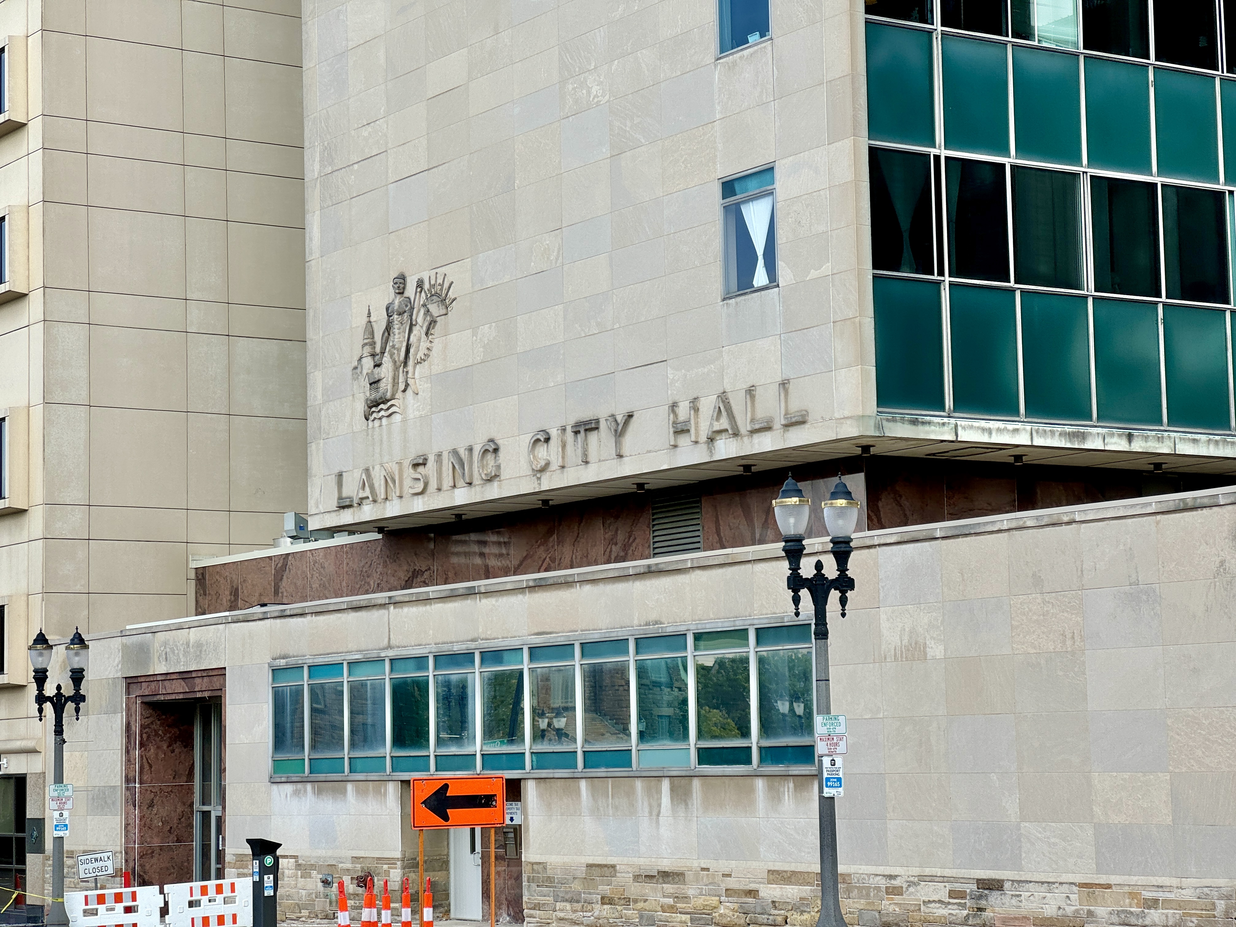 Limestone facade of Lansing City Hall with carved building name and glass tower above.