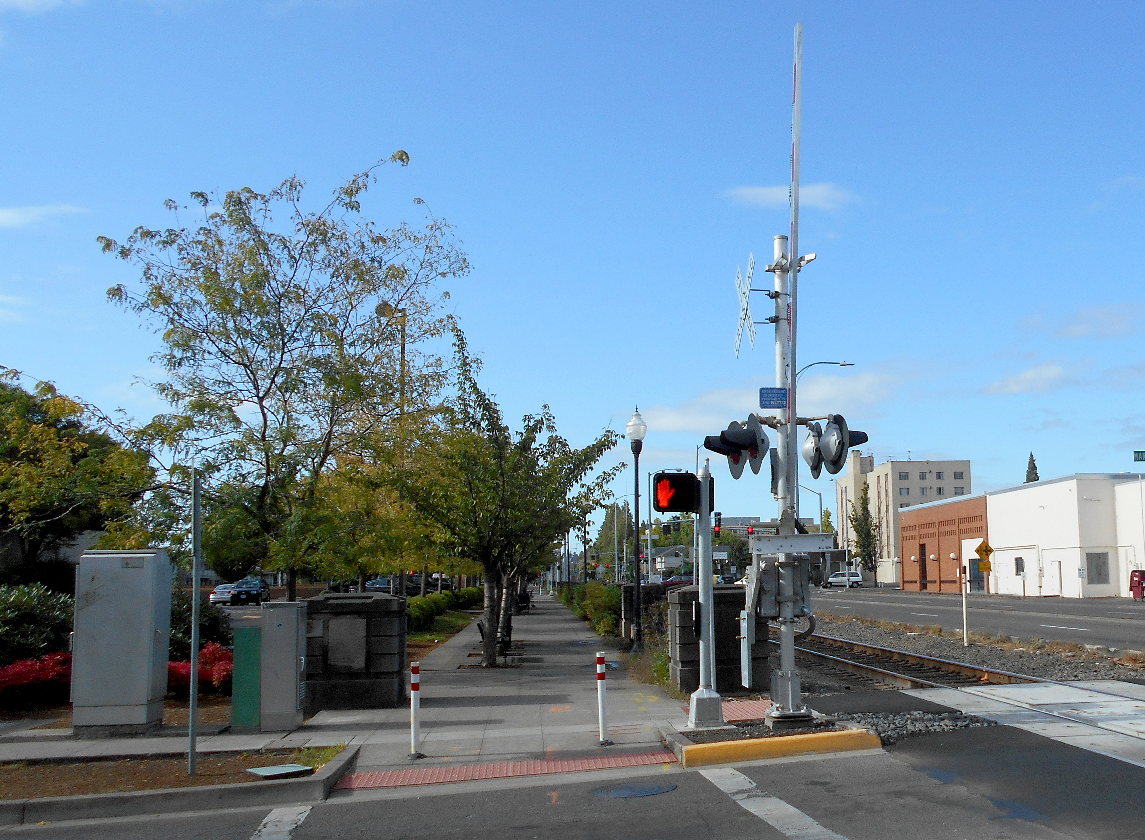Railroad crossing with red signal lights, gates, and warning pole against a blue sky.