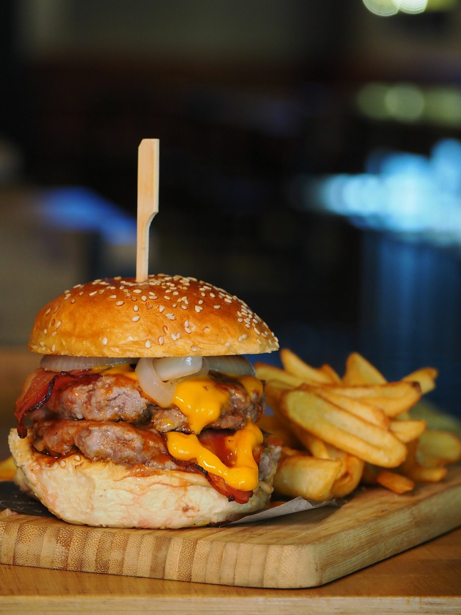 A double cheeseburger with bacon and fries served on a wooden cutting board.